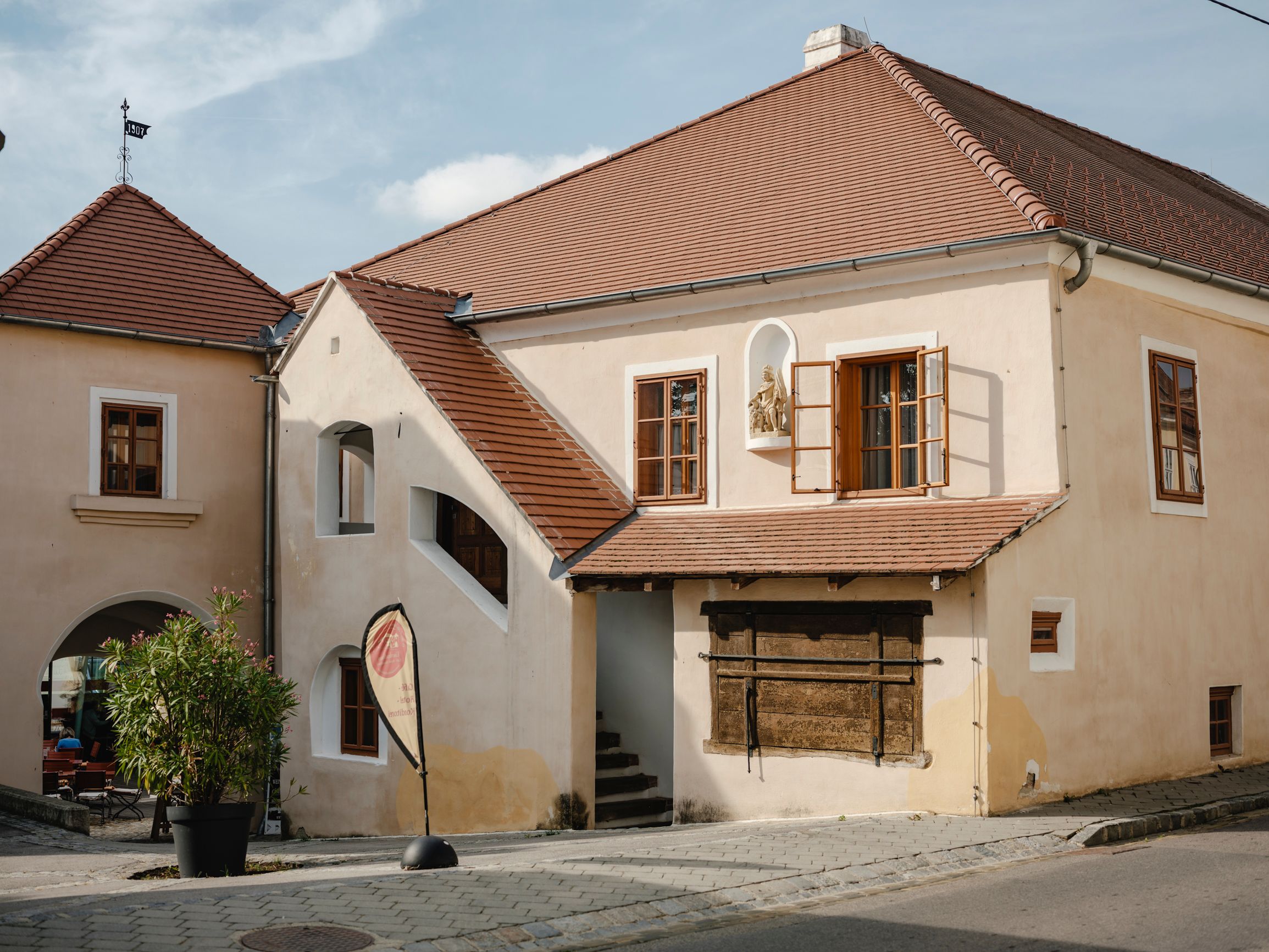 Historická budova s červenými taškovými střechami a otevřenými okny.