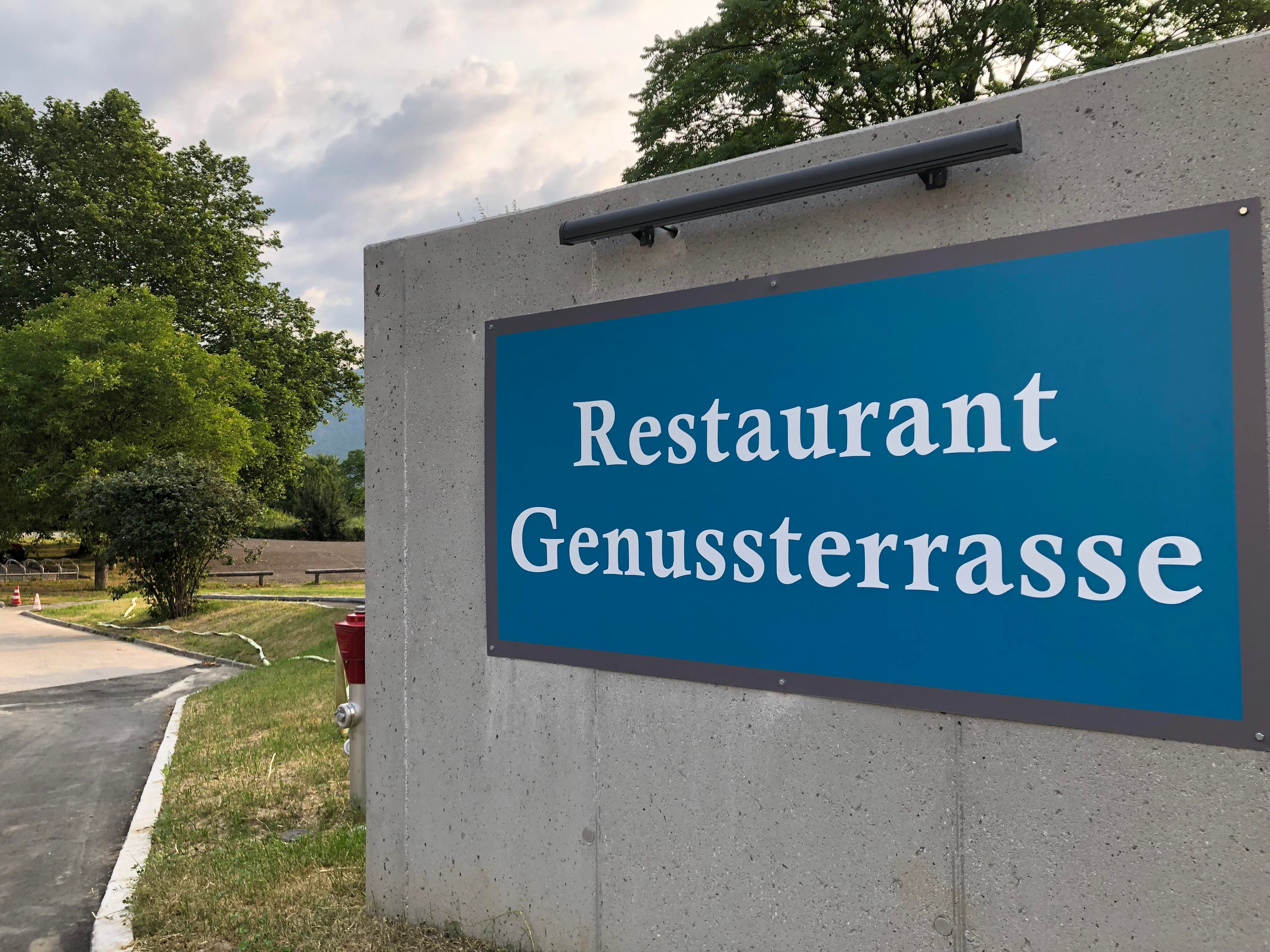 Nápis na restauraci "Genussterrasse" na betonové zdi venku.