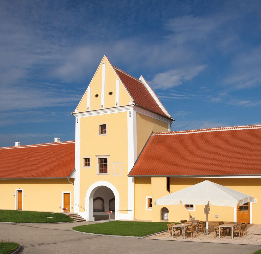 Žlutá budova s červenou střechou a obloukem, v pozadí modrá obloha.