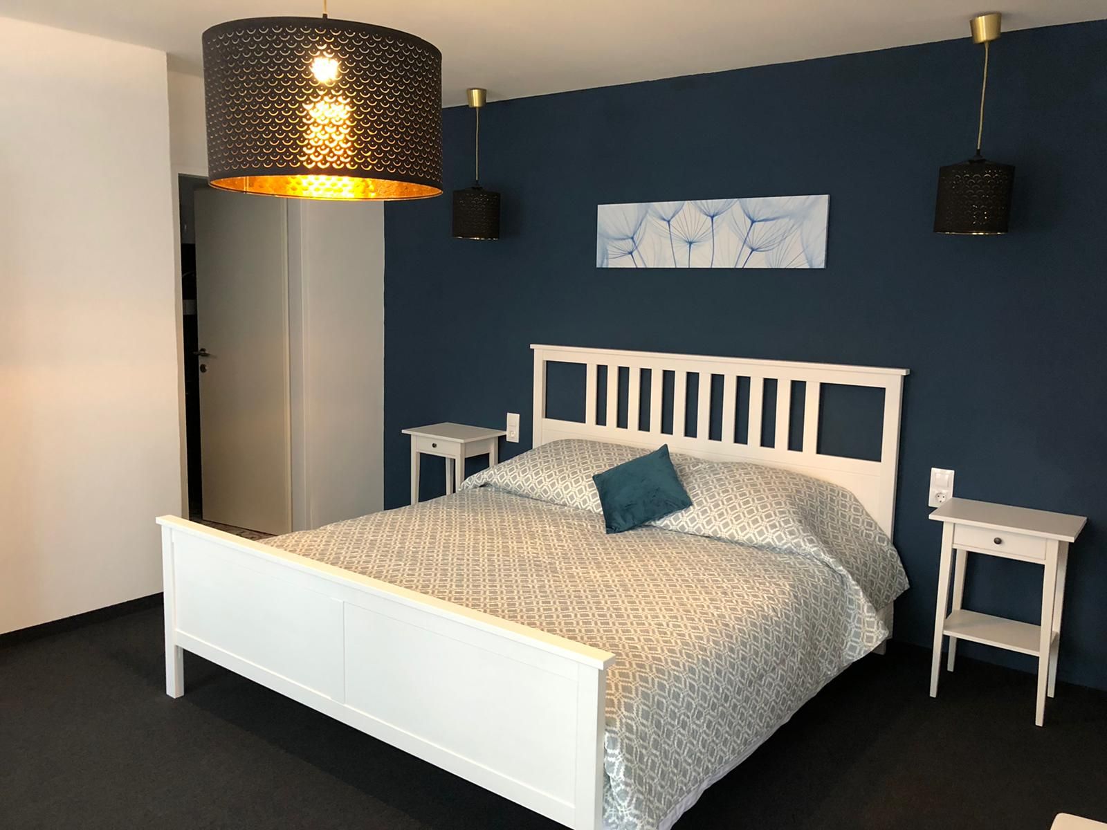 Moderní dvoulůžkový pokoj s bílou postelí, modrou stěnou a stylovými lampami.