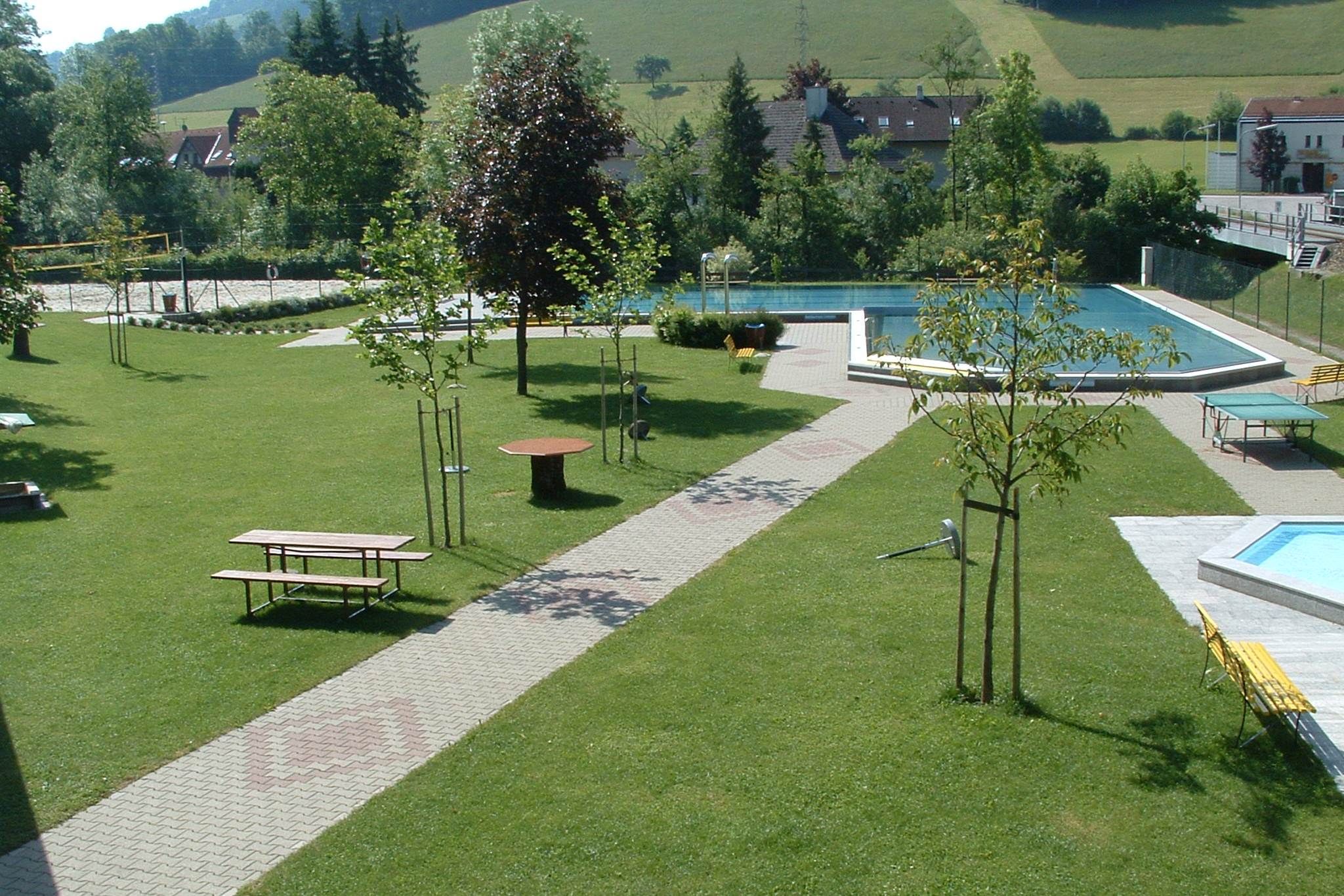 Zelený park s bazénem a lavičkami.