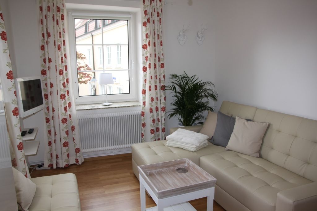 Světlý obývací pokoj s béžovou pohovkou, polštáři, konferenčním stolkem a oknem se závěsy.