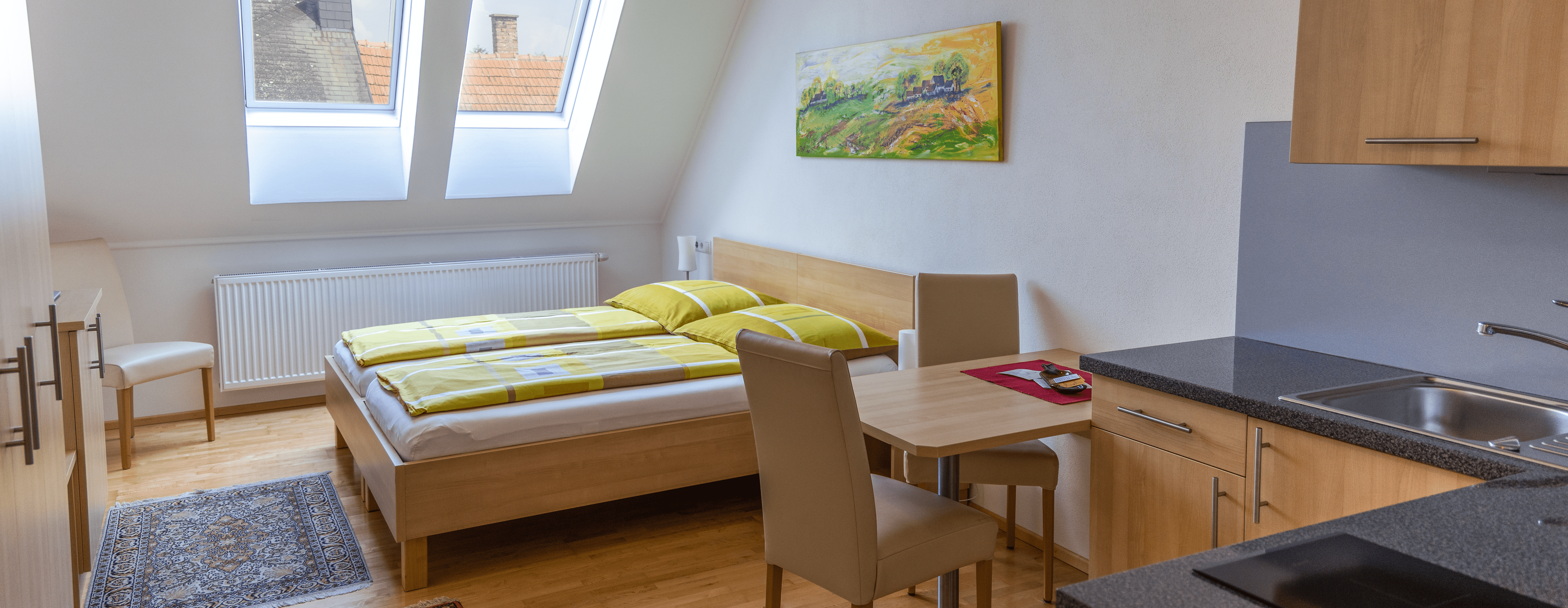 Dvoulůžkový pokoj s kuchyňským koutem, postelí, stolem a židlemi.