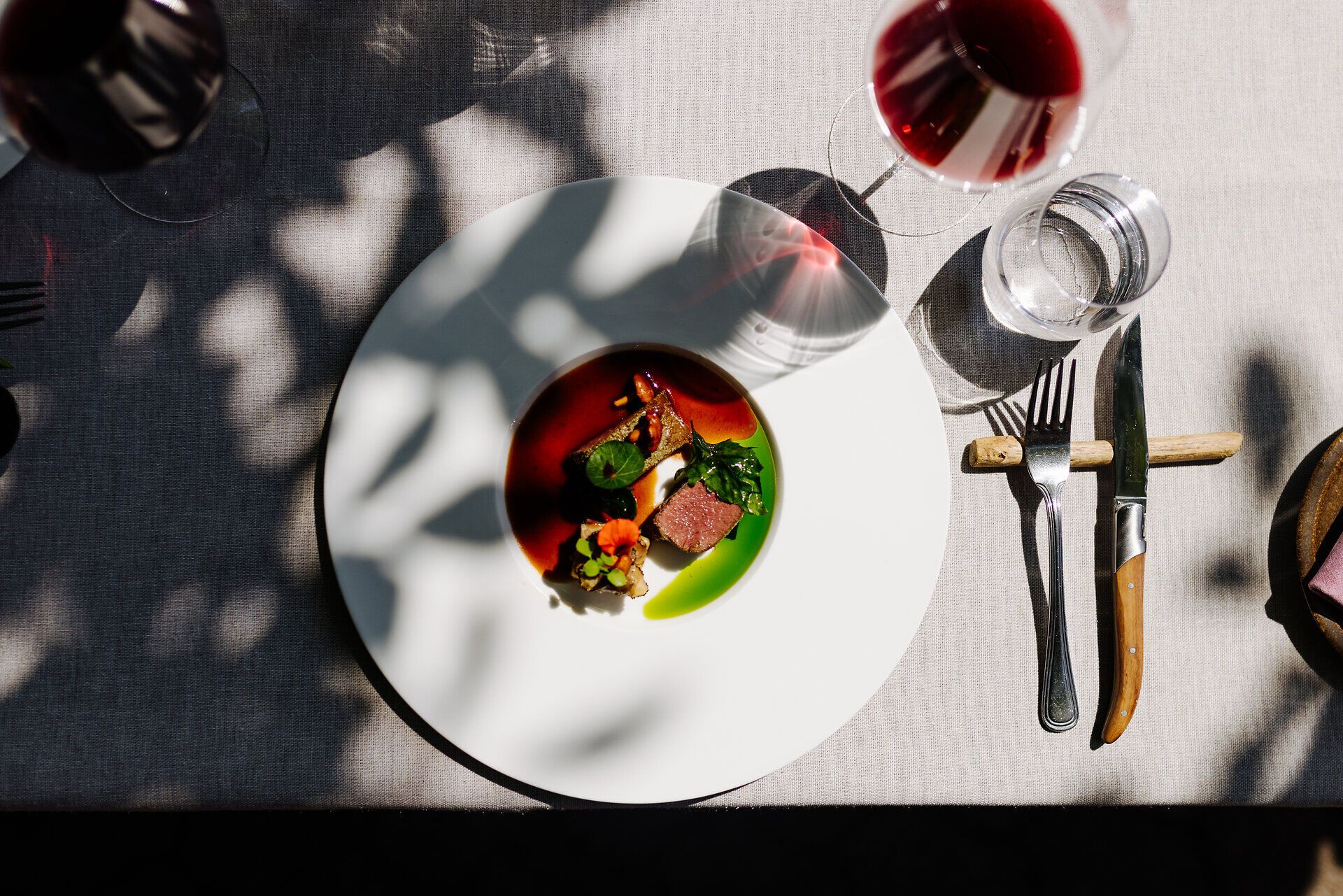 Ein kunstvoll angerichteter Teller mit regionalen Köstlichkeiten lädt zum Genießen ein. Umgeben von sanften Schatten und dem Glanz von Rotwein, vermittelt die Szenerie ein Gefühl von Gemütlichkeit und Genuss. Hier wird die Liebe zur Natur und zur Kulinarik spürbar.