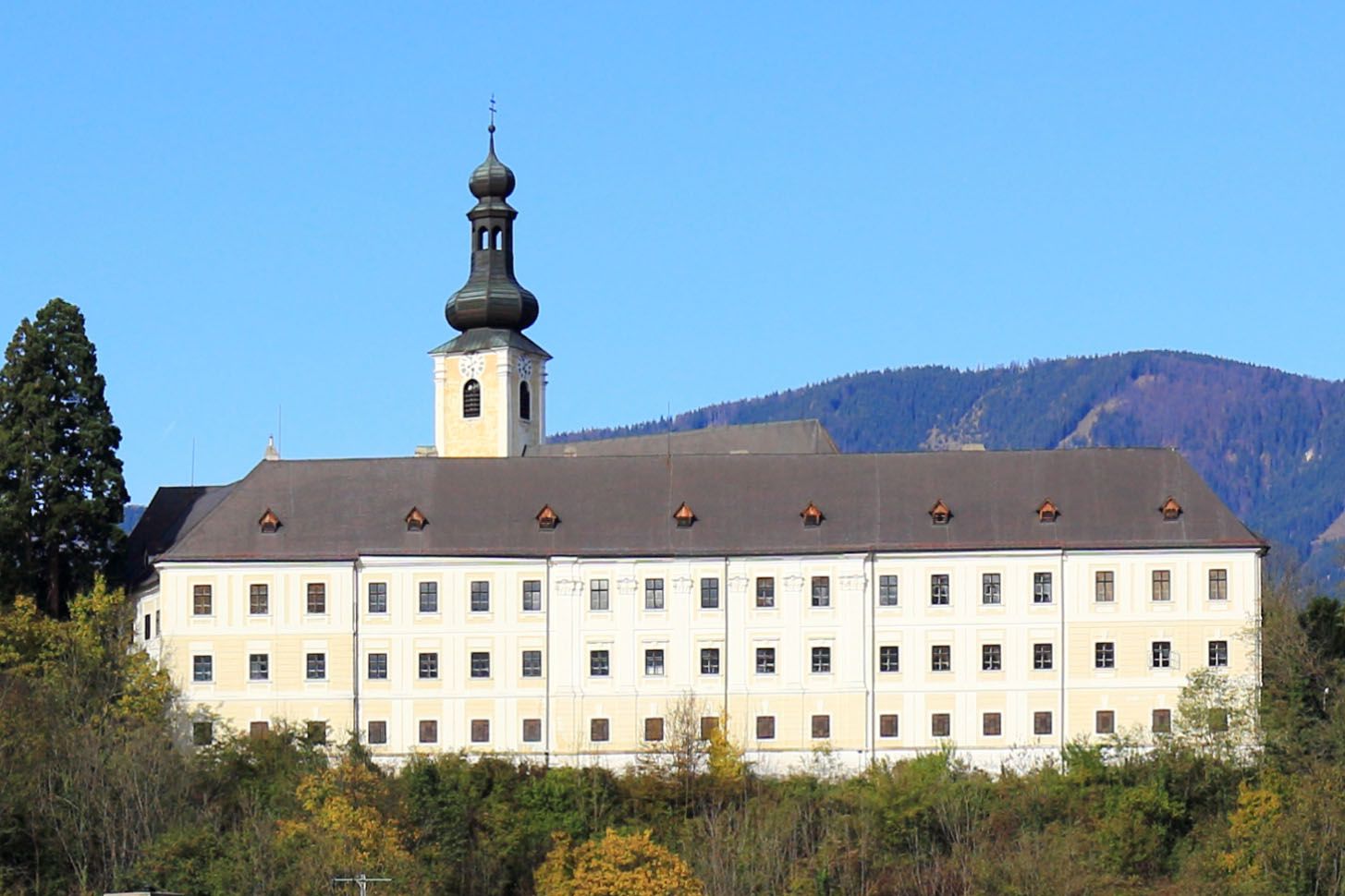 Hrad Gloggnitz před zalesněnými kopci a modrou oblohou.
