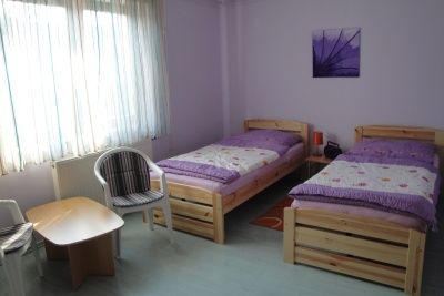 Jednoduše zařízený pokoj se dvěma samostatnými lůžky, malým stolkem a dvěma židlemi.