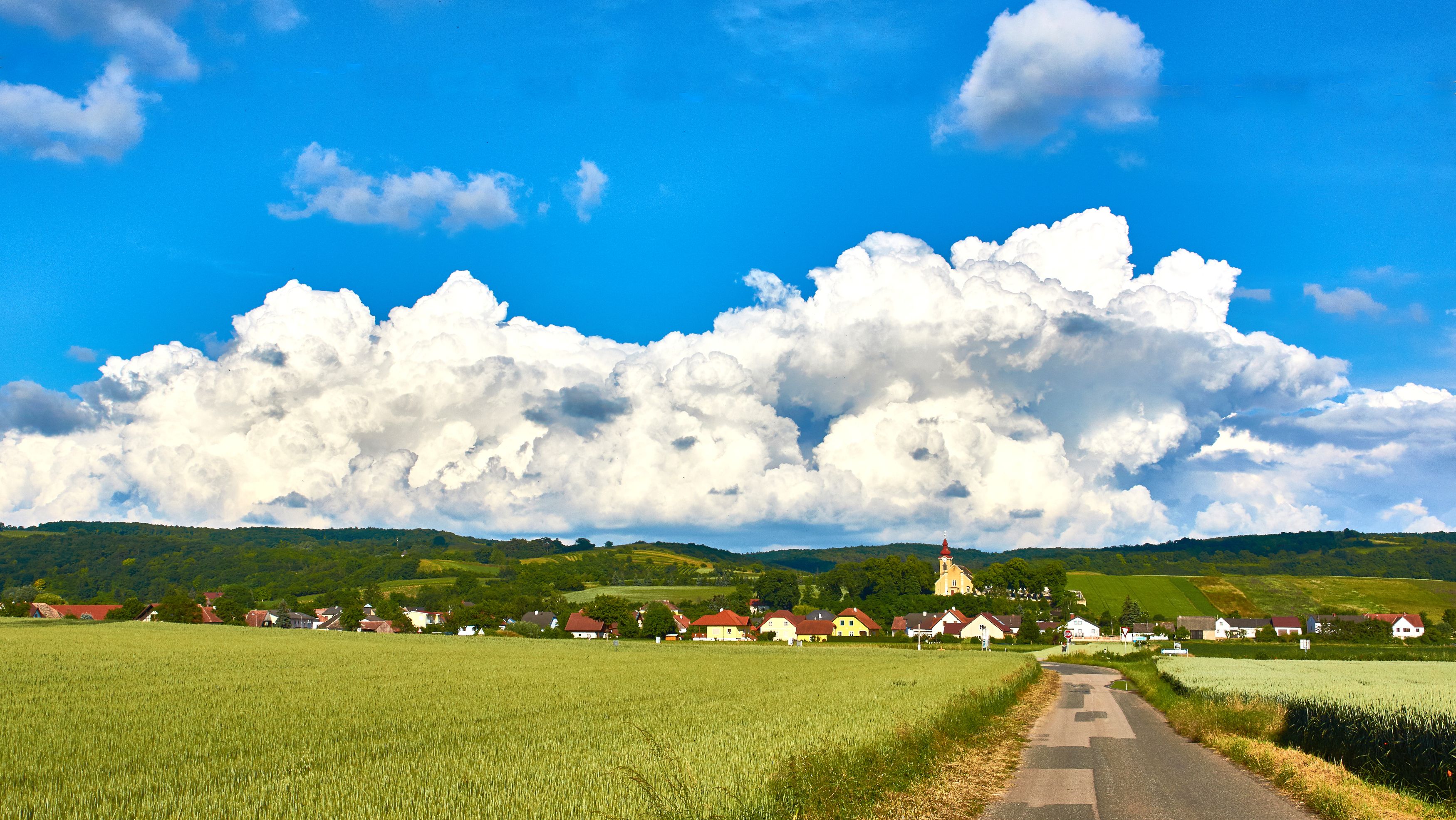 Krajina s vesnicí, poli a kostelem před velkými mraky.