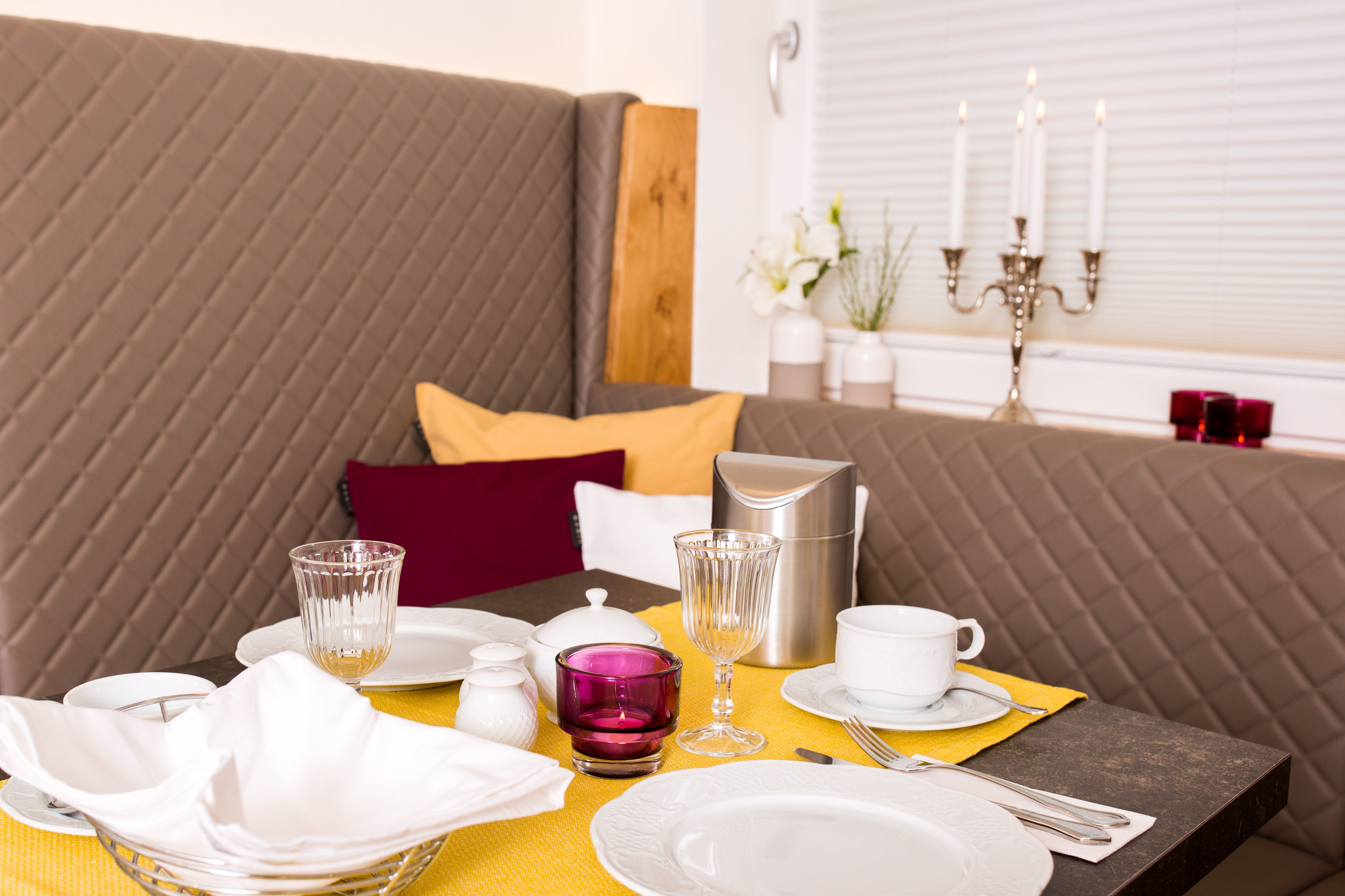 Elegantní snídaňový stůl se žlutým běhounem, nádobím, sklenicemi a svícny.