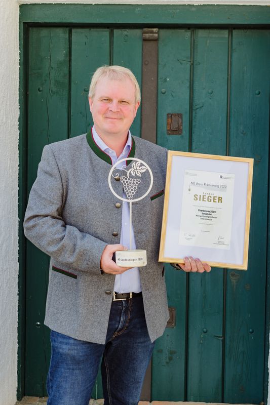Osoba držící Ocenění a certifikát před zelenými dřevěnými dveřmi.