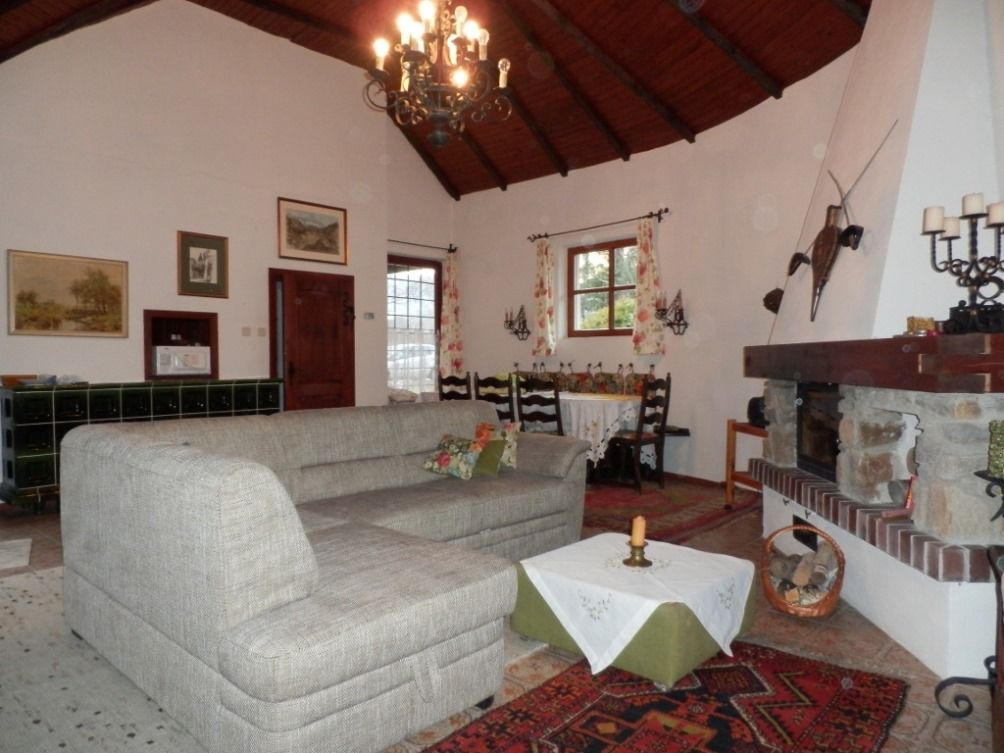 Útulný obývací pokoj s šedou pohovkou, krbem a jídelním stolem. Rustikální dekorace a dřevěný trámový strop.