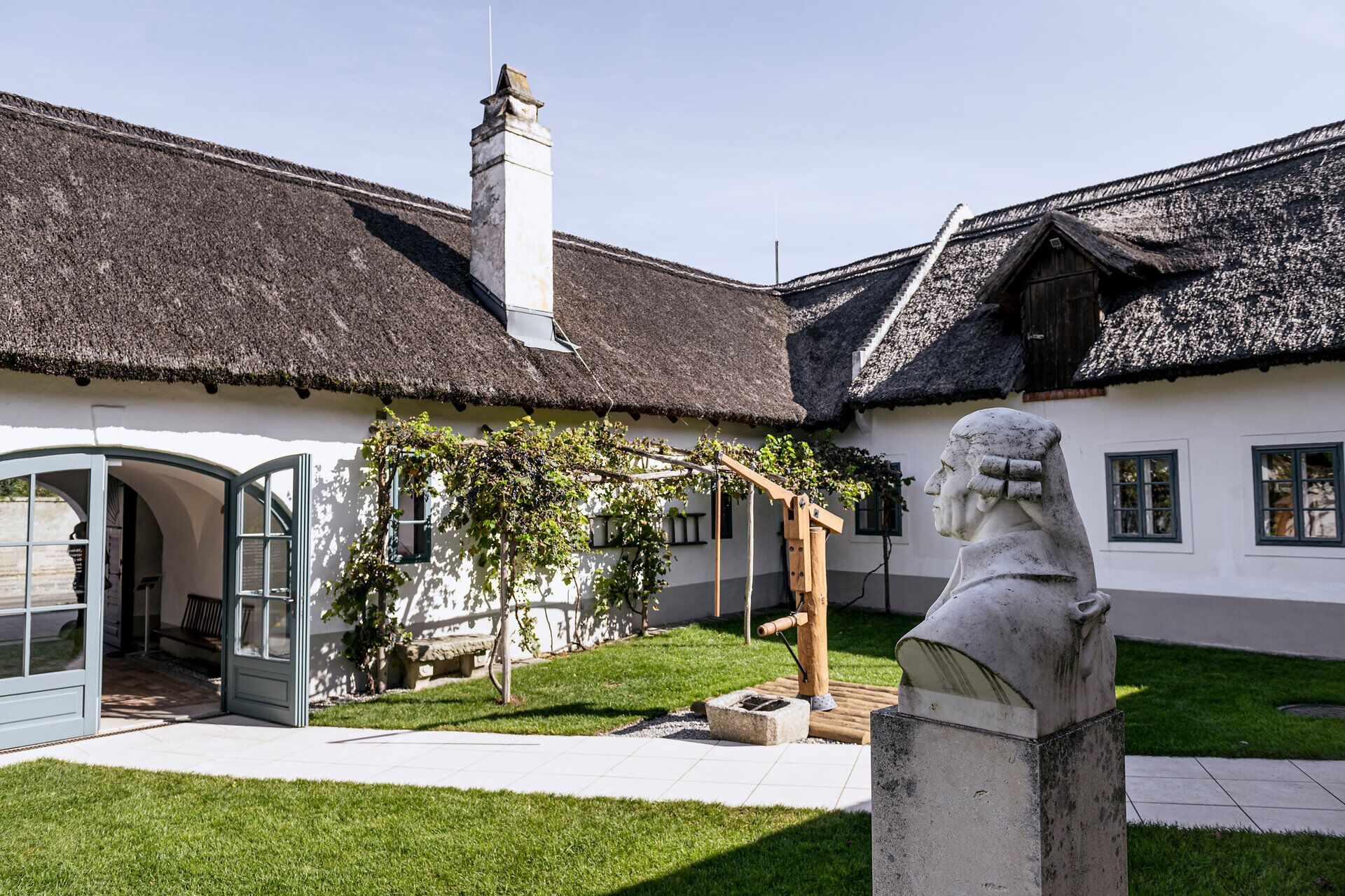 Vnitřní nádvoří Haydnova rodného domu s doškovými střechami a Haydnovou bustou.