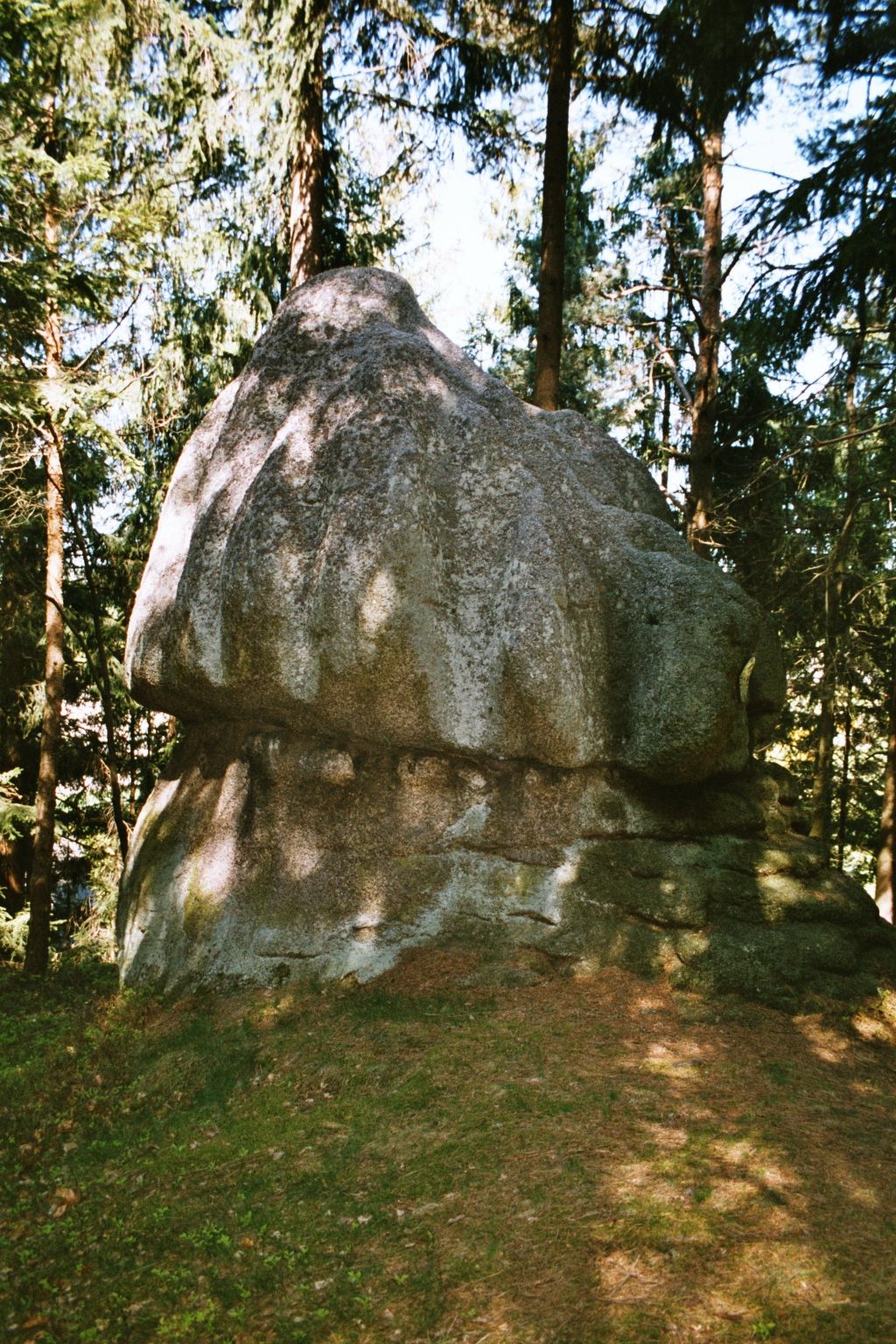 Velká kulatá skála v lese, obklopená stromy.
