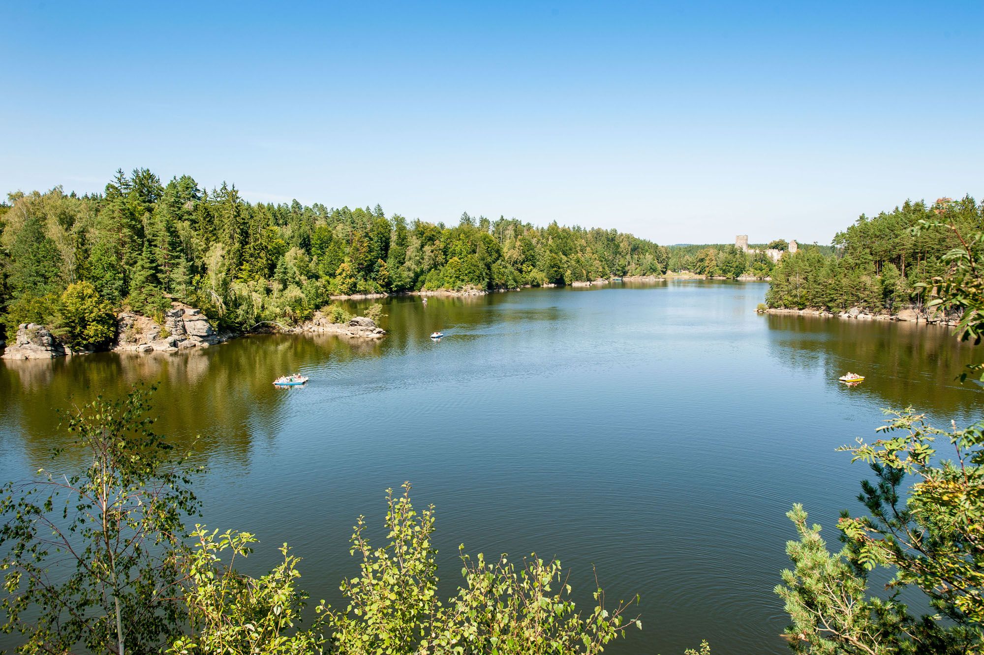 Klidné jezero s okolními lesy a několika loděmi na vodě.