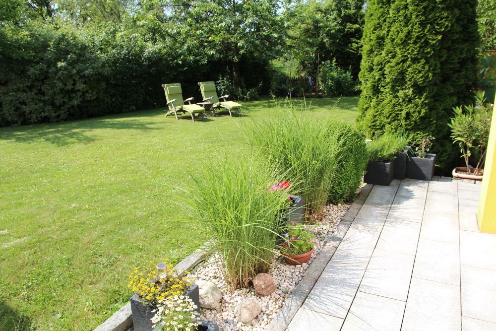 Zahrada s trávníkem, lehátky a osázeným okrajem.
