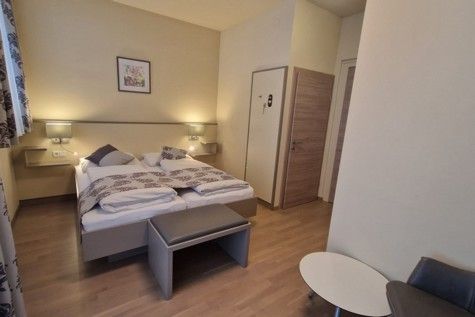 Hotelový pokoj s manželskou postelí, dřevěnou podlahou a moderním nábytkem.