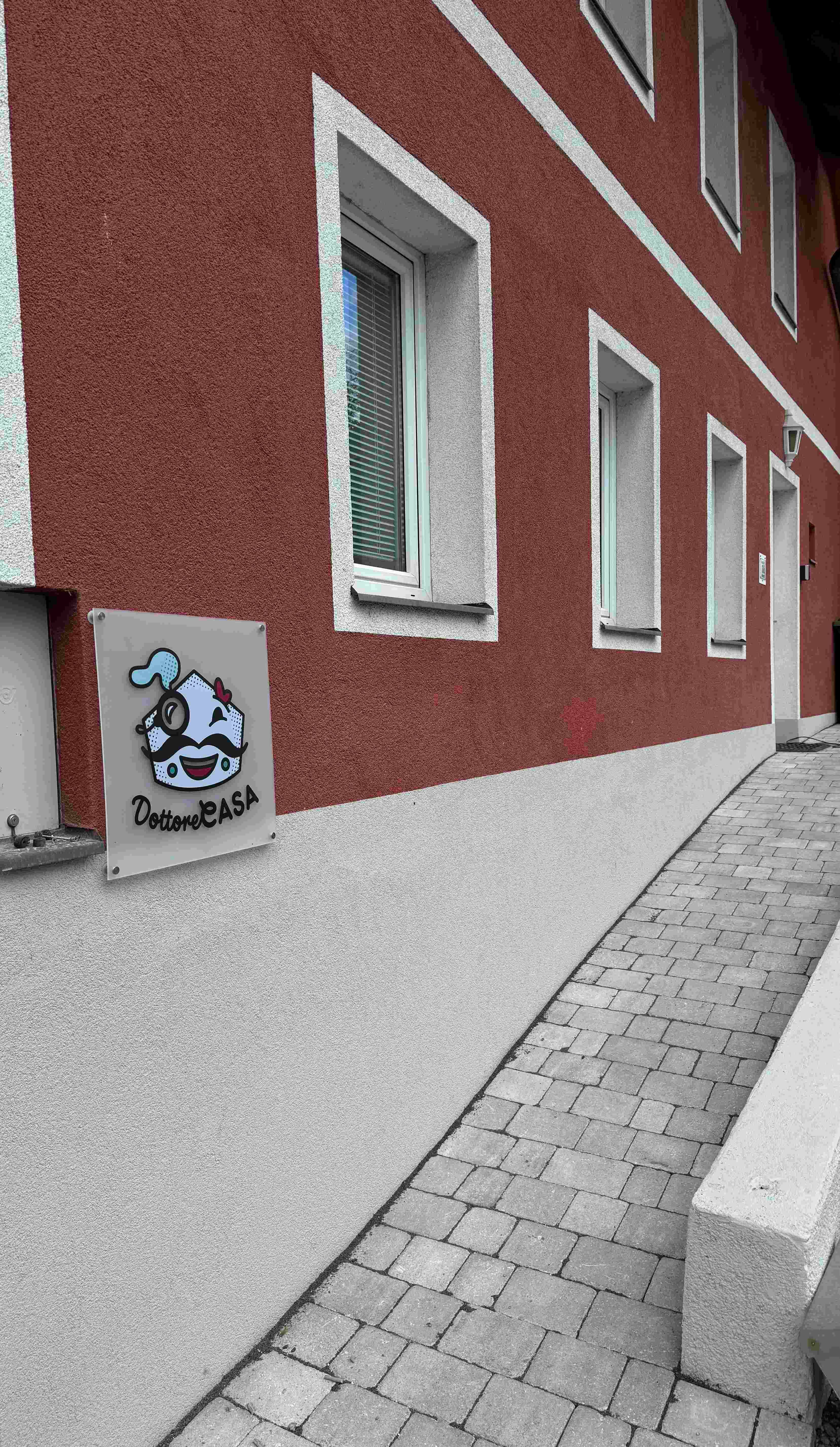 Pohled zvenčí na budovu s červenou fasádou a nápisem "Dottore Casa".