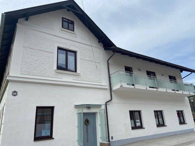 Dvoupodlažní bílý dům s balkonem a několika okny.