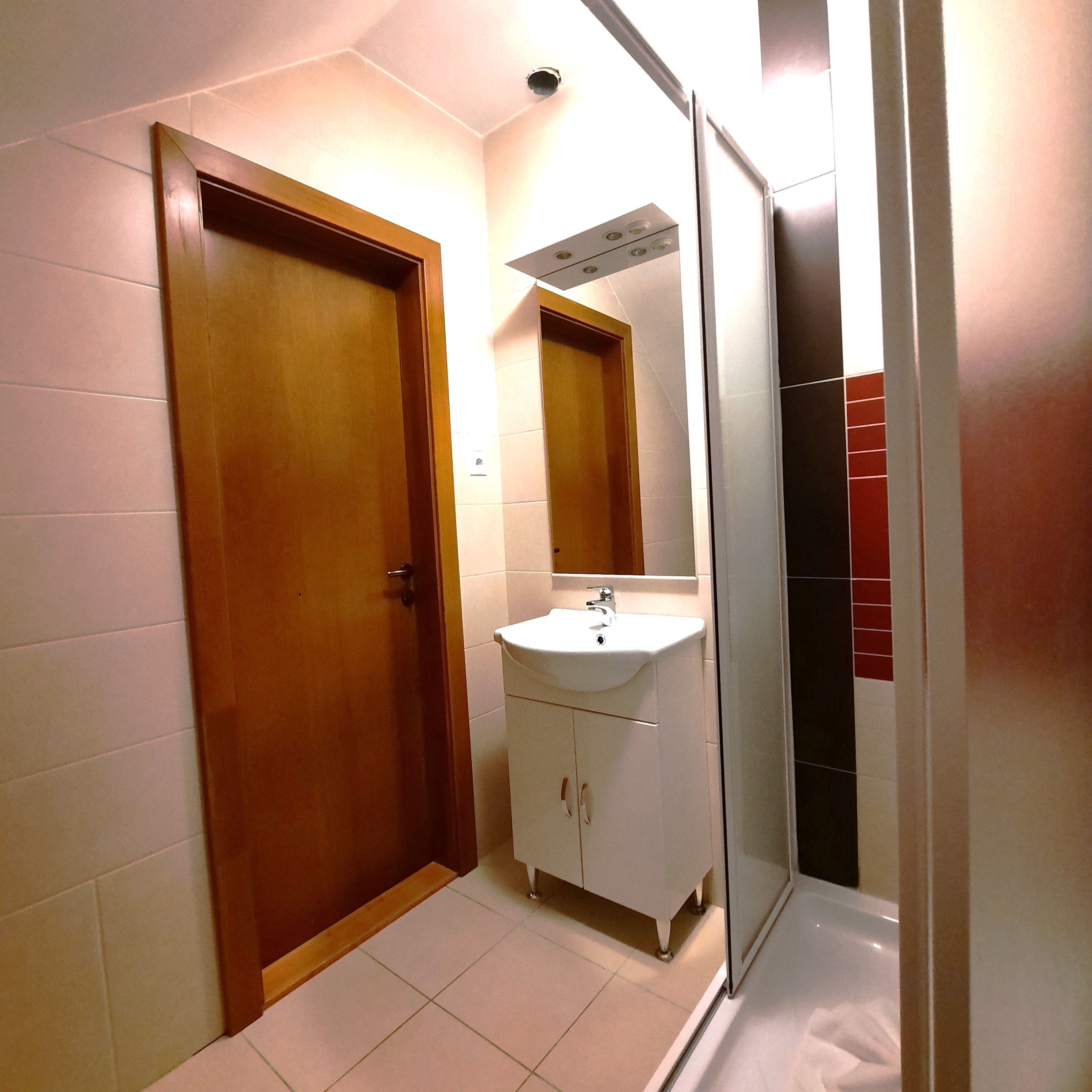 Moderní koupelna s dřevěnými dveřmi, umyvadlem a sprchovým koutem.