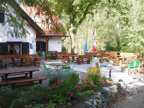 Venkovní prostor chaty Schindlhütte se stoly a židlemi v zeleni.