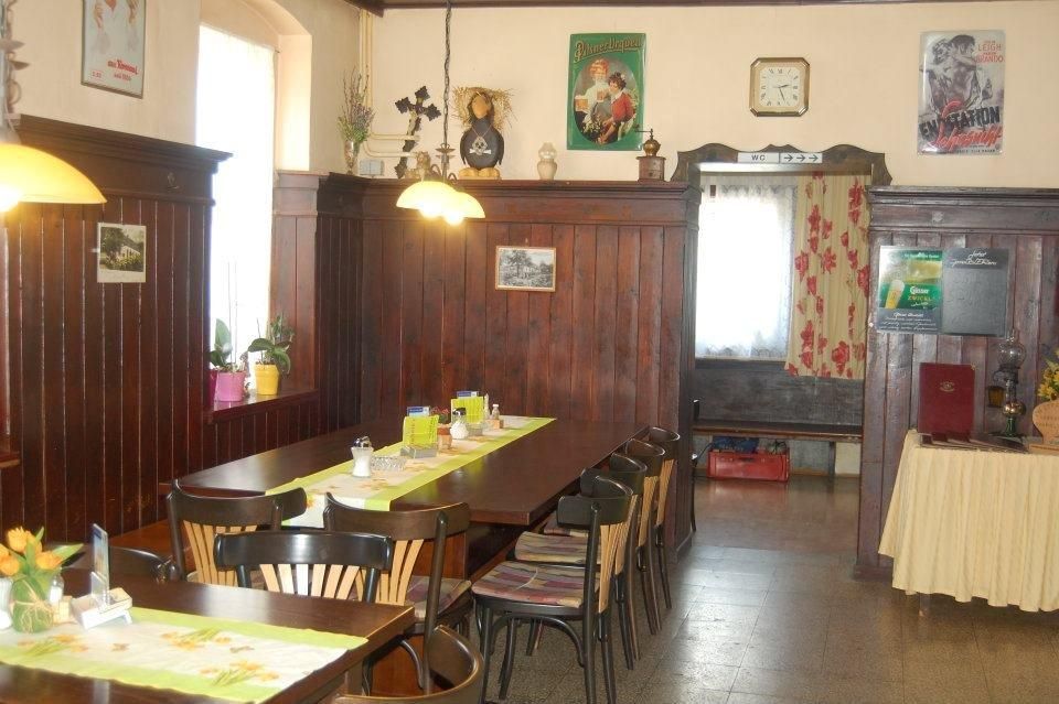 Útulná jídelna s dřevěným obložením, stolem a židlemi, dekorativními plakáty a hodinami na stěně.