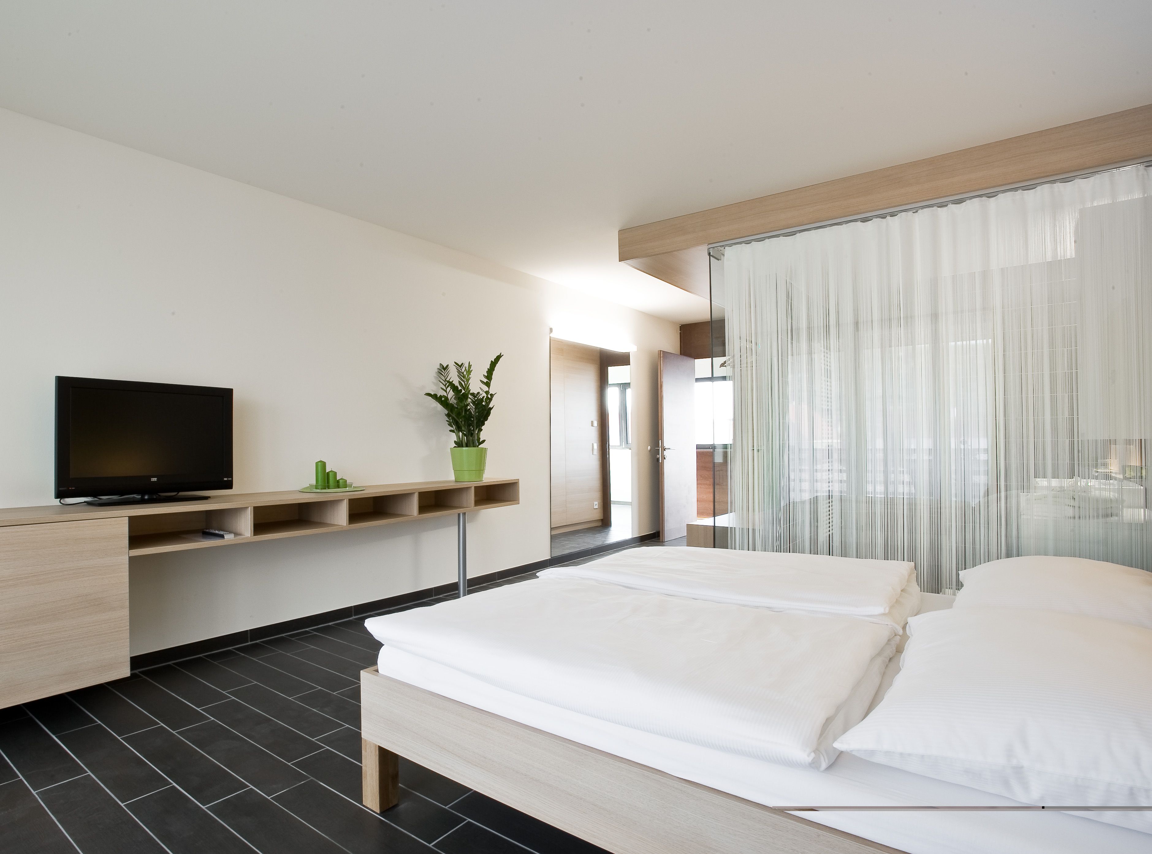 Moderní hotelový pokoj s manželskou postelí, televizí a rostlinami.