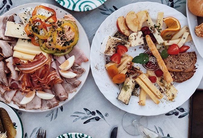 Dva talíře s uzeninami, sýrem, zeleninou a ovocem na stole.