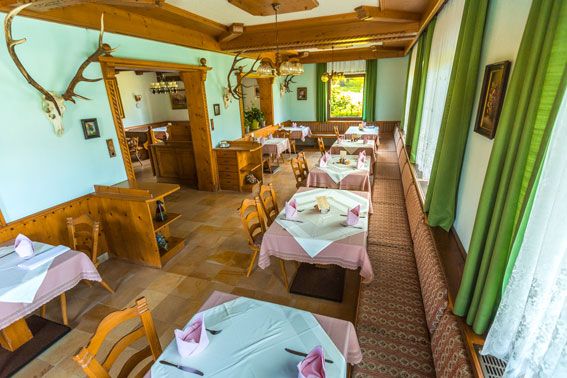 Útulná restaurace s dřevěným nábytkem a ubrusy, zdobená parožím na stěnách.
