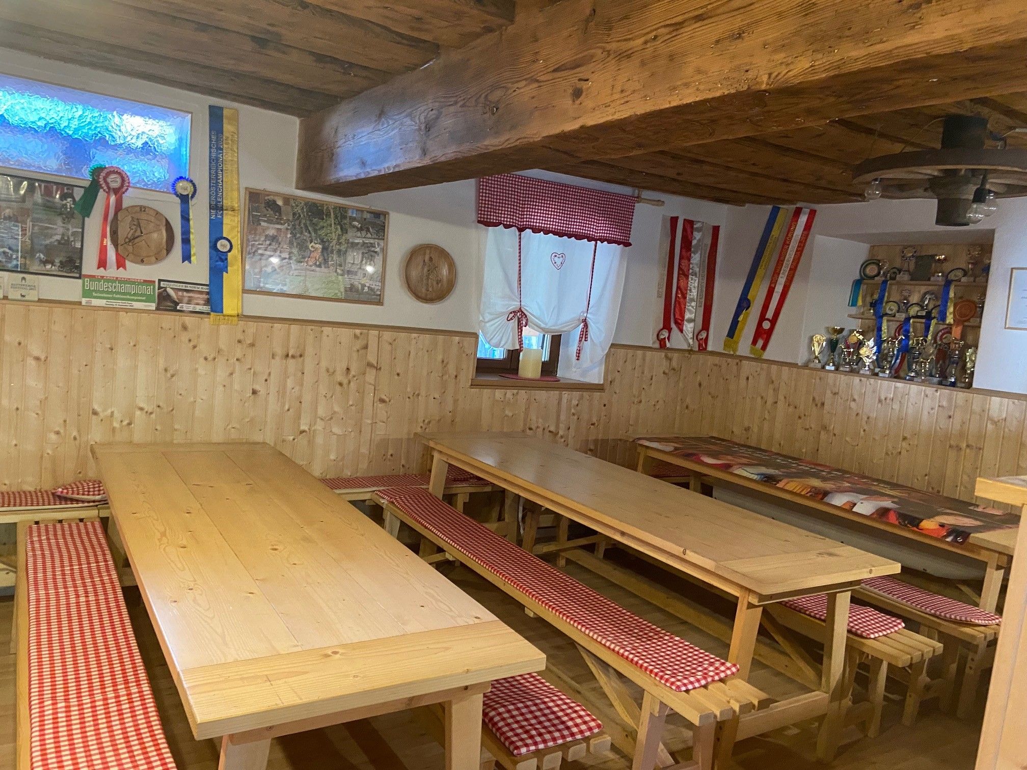 Útulná společenská místnost s dřevěnými stoly, lavicemi a dekoracemi na stěnách.