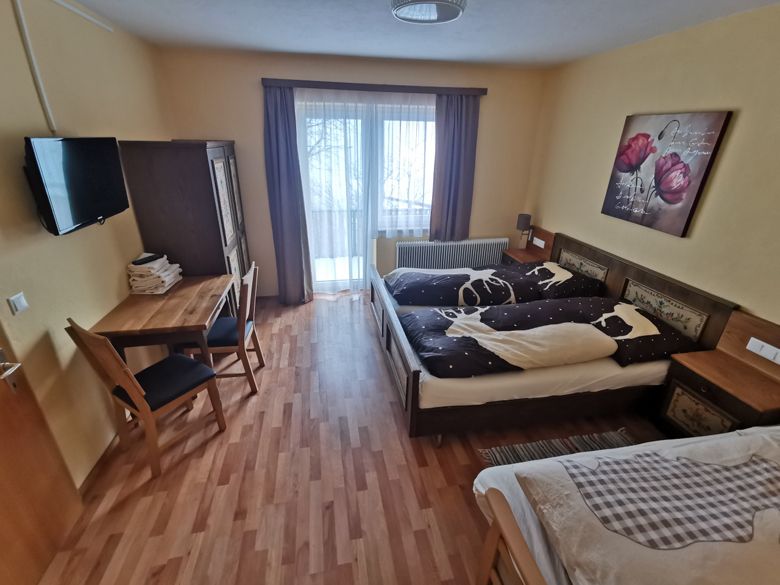Útulná ložnice s manželskou postelí, stolem, židlemi a balkonem.