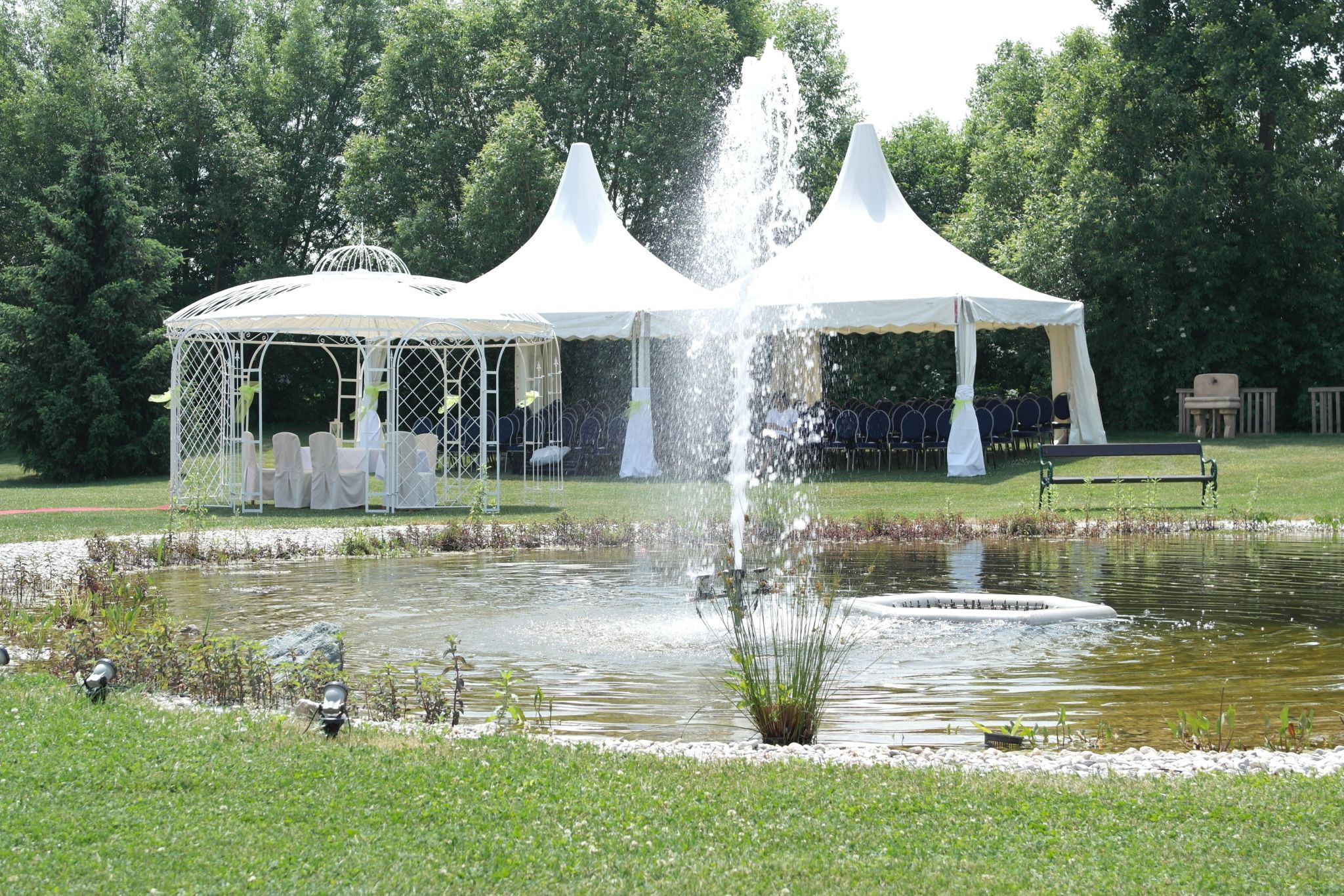 Svatební pavilon a stany u rybníka s fontánou v zahradě.