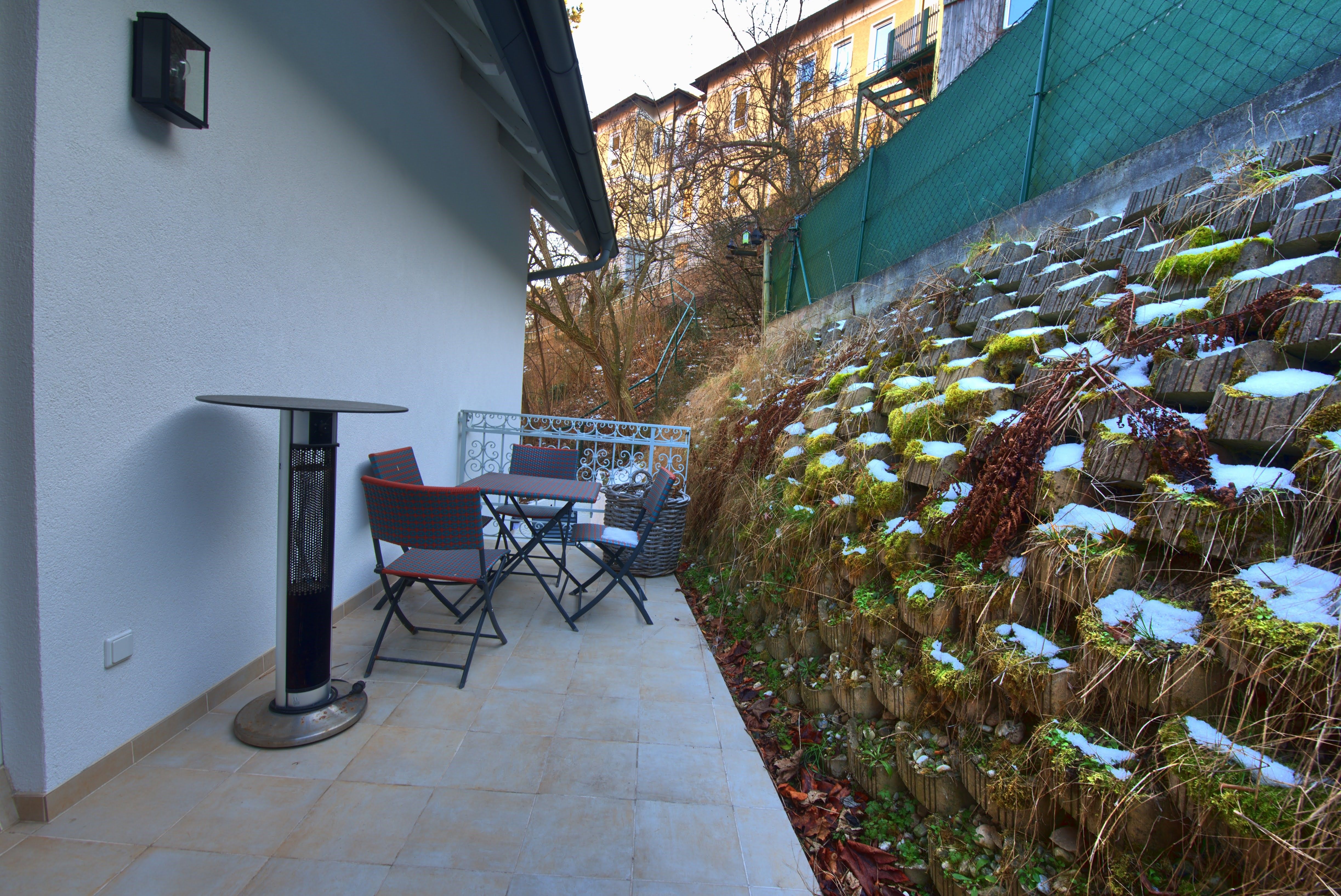 Terasa se stolem, židlemi a sálavým topením u zelené stěny.