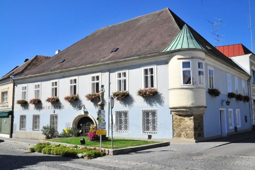 Historická budova s modrou fasádou a květinovými truhlíky, muzeum místní historie Langenlois.