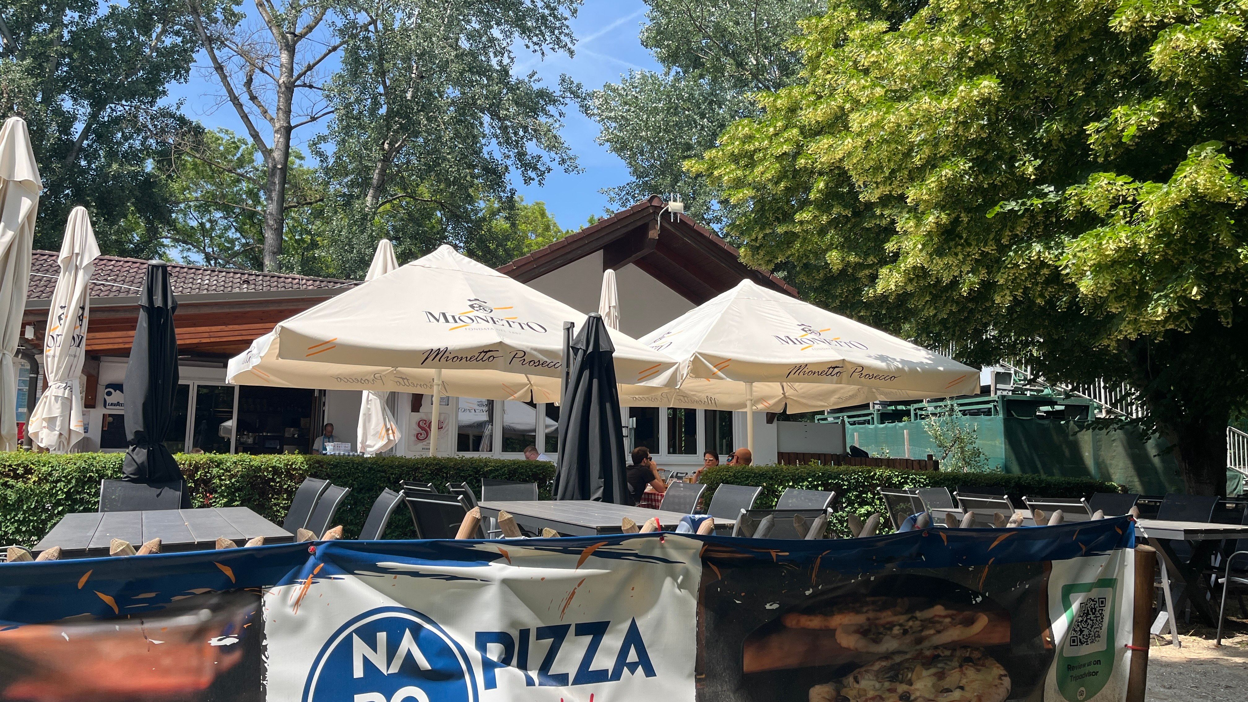 Zahrada pro hosty s výhledem na budovu pizzerie, v pozadí stromy.