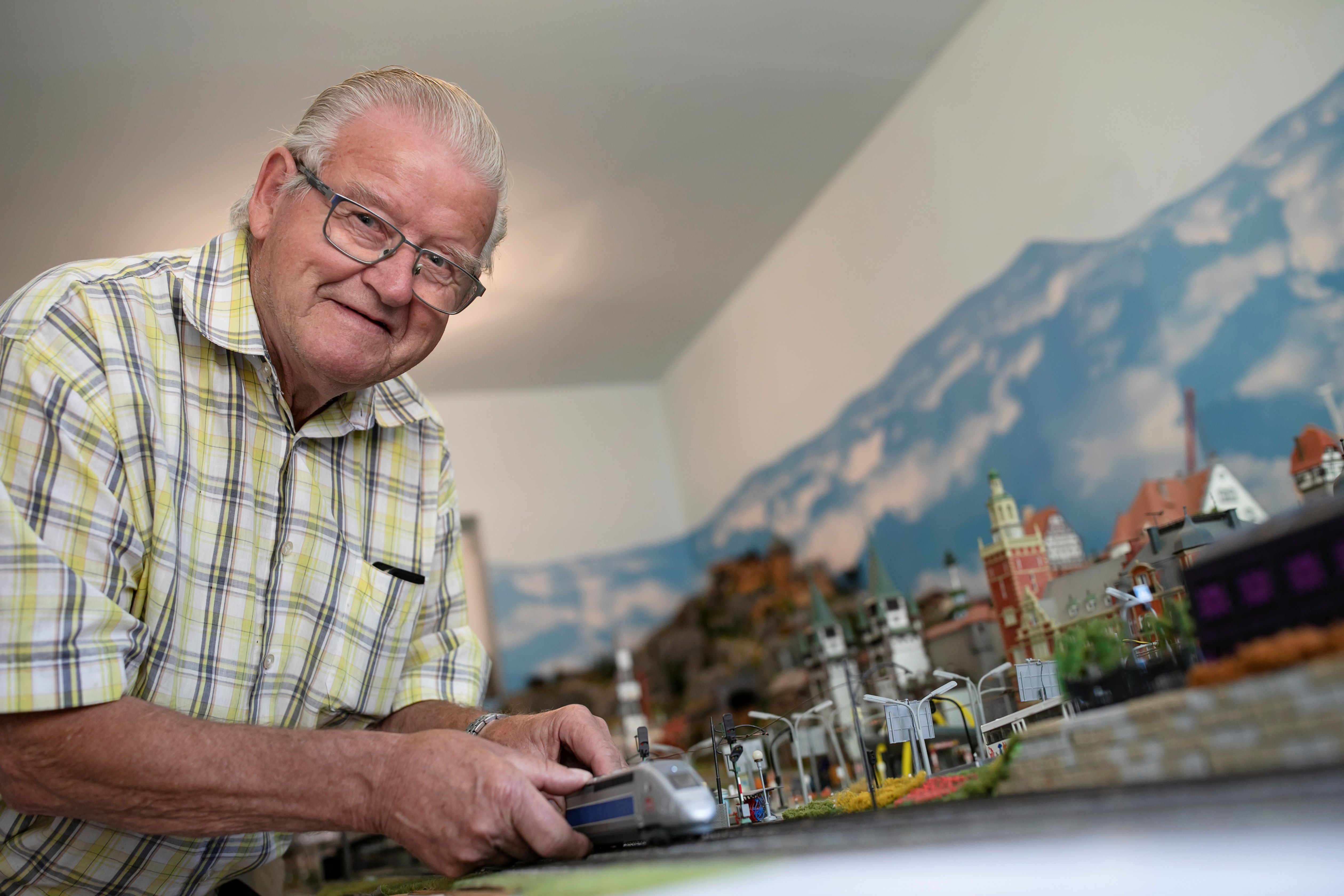 Dědeček Moser stojí před svým modelovým železničním kolejištěm a ukazuje lokomotivu. 