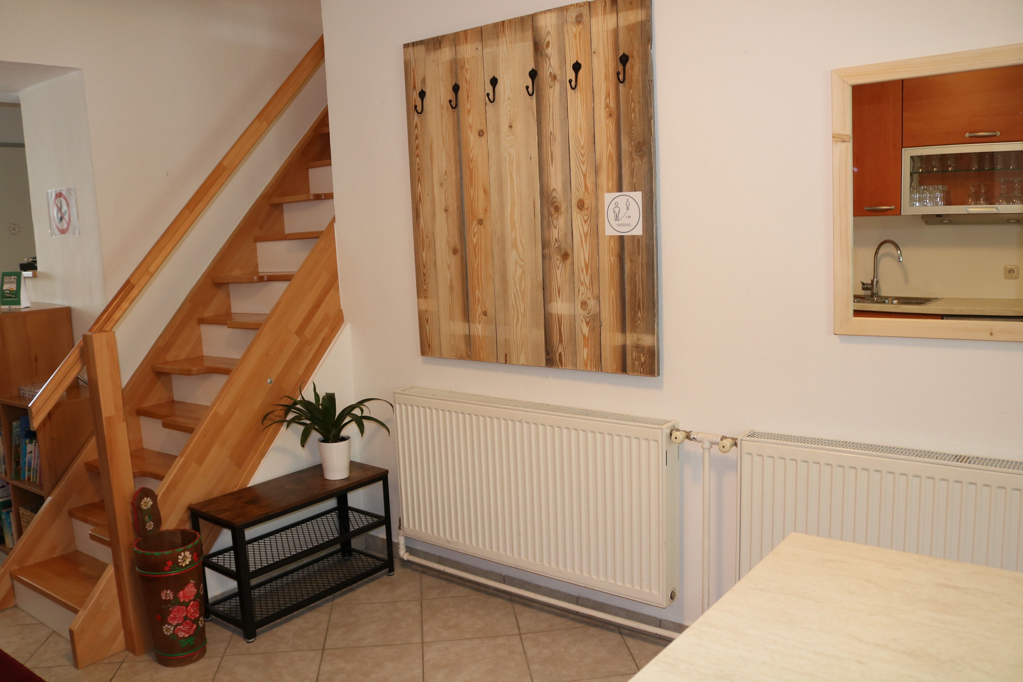 Interiér s dřevěným schodištěm, skříní, rostlinou a kuchyňským oknem.