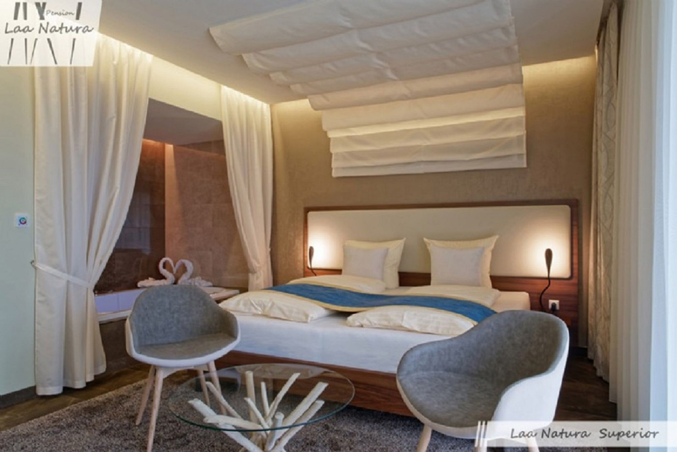 Moderní dvoulůžkový pokoj s velkou postelí, dvěma šedými židlemi a skleněným stolem.