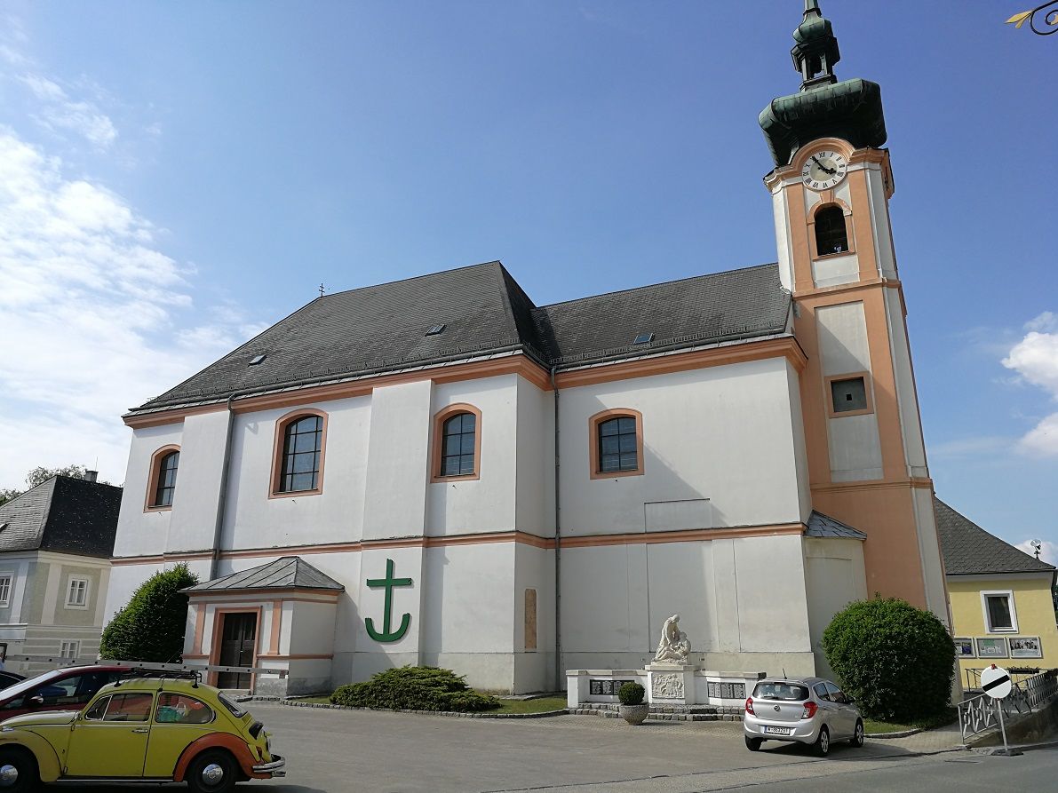 Farní kostel Würmla s věžními hodinami a zaparkovanými auty.