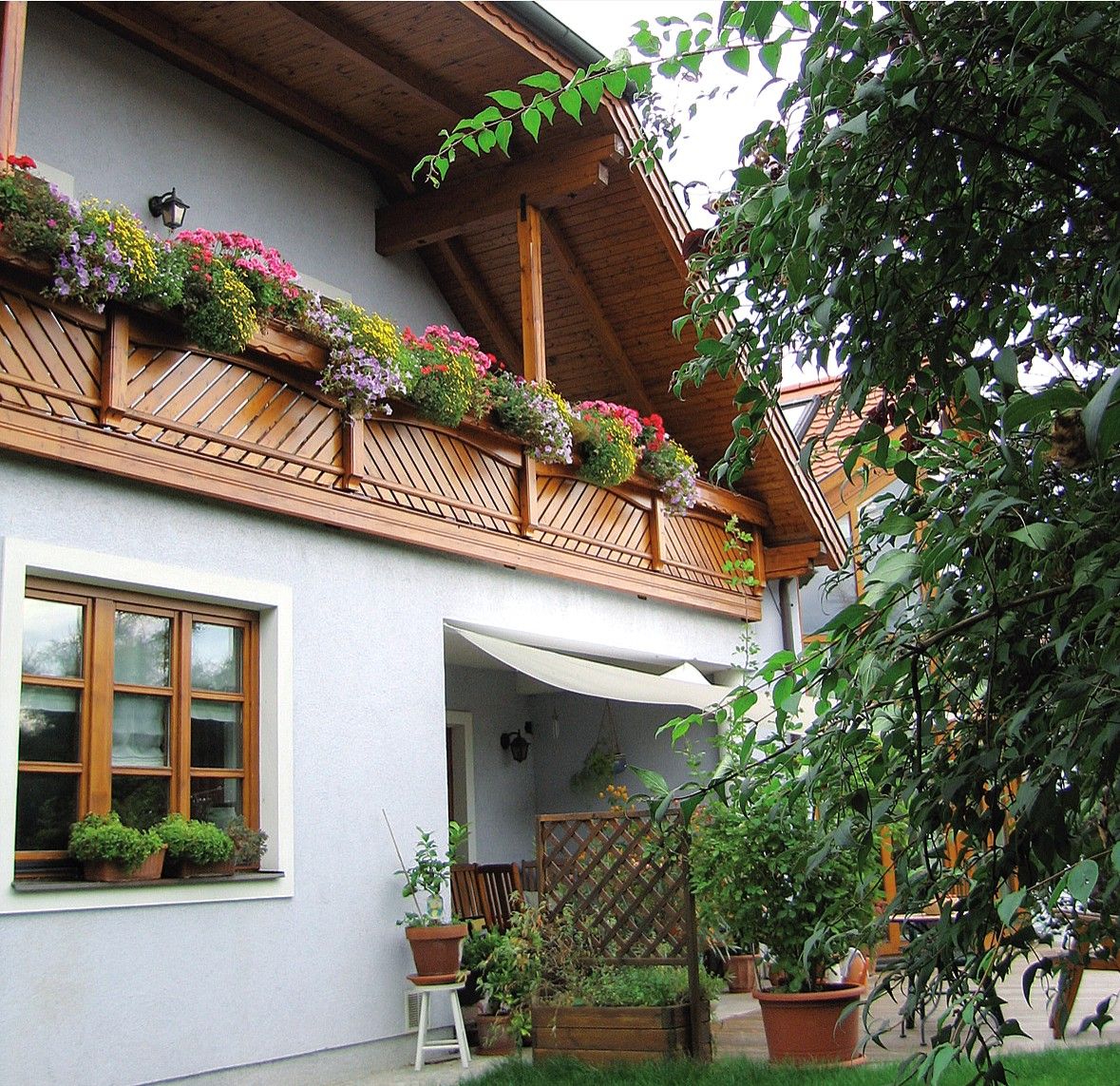 Penzion s dřevěným balkonem a rozkvetlými květinami, obklopený zelení.