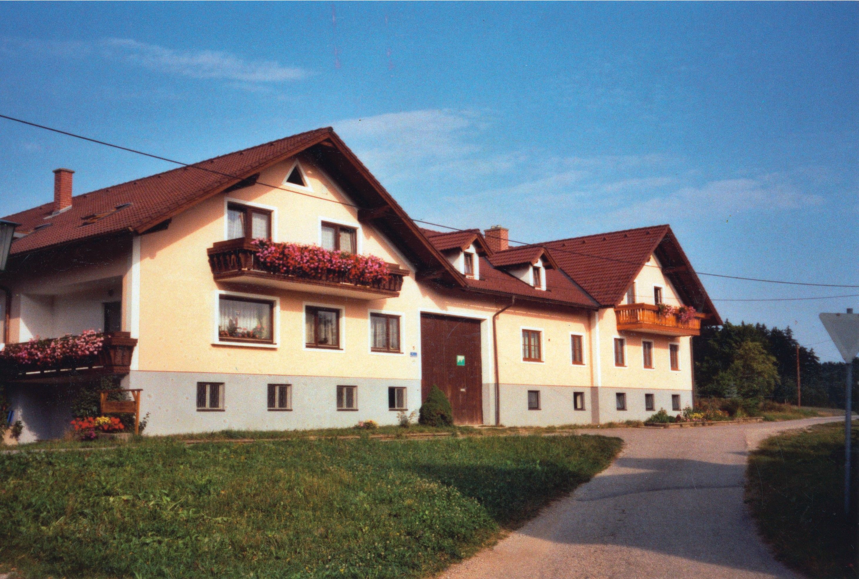 Velký dvoupatrový statek s červenými střechami a květinovými truhlíky na balkonech.