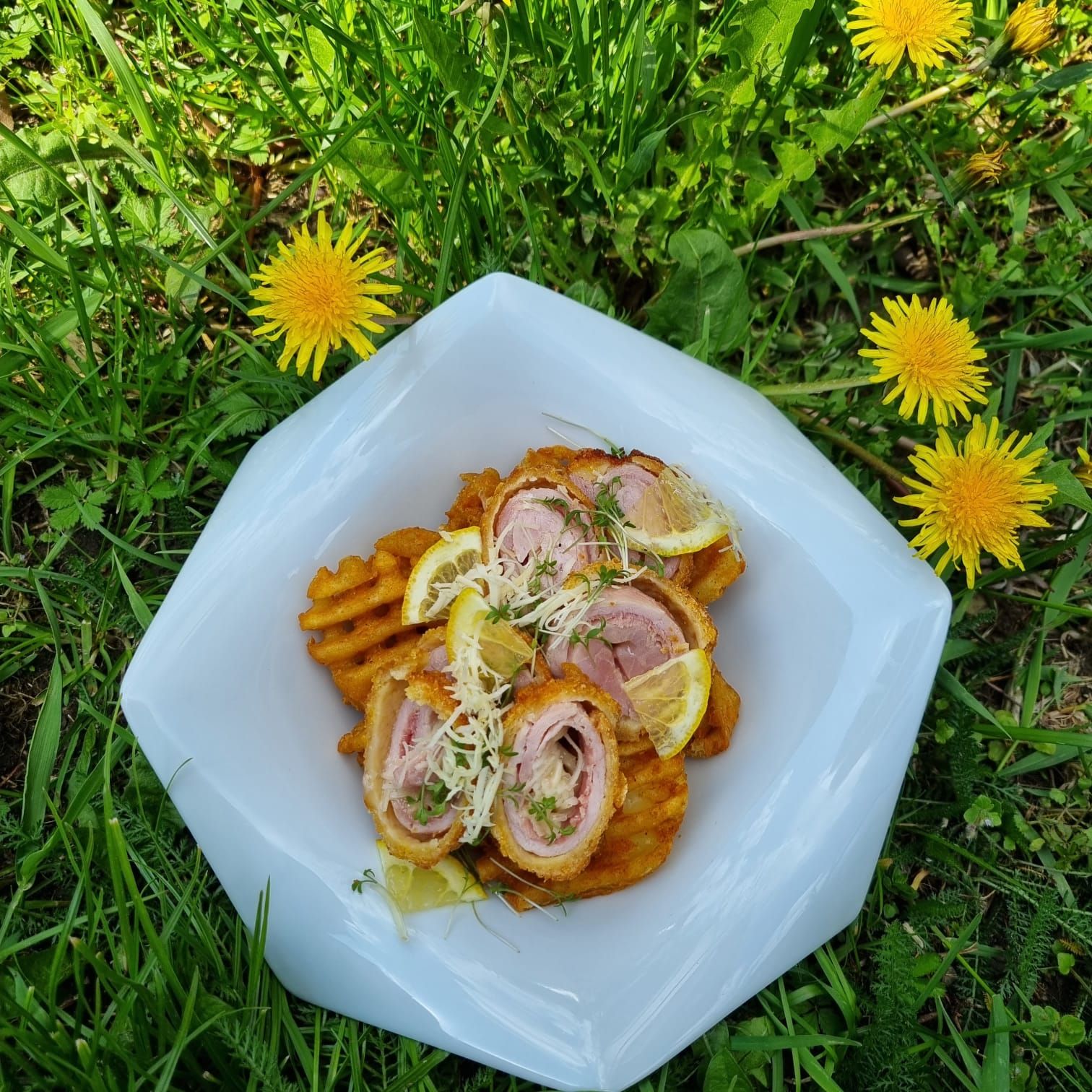 Na louce s pampeliškami leží talíř s kordonovými rohlíčky a vaflovými hranolky, ozdobený plátky citronu a řeřichou.