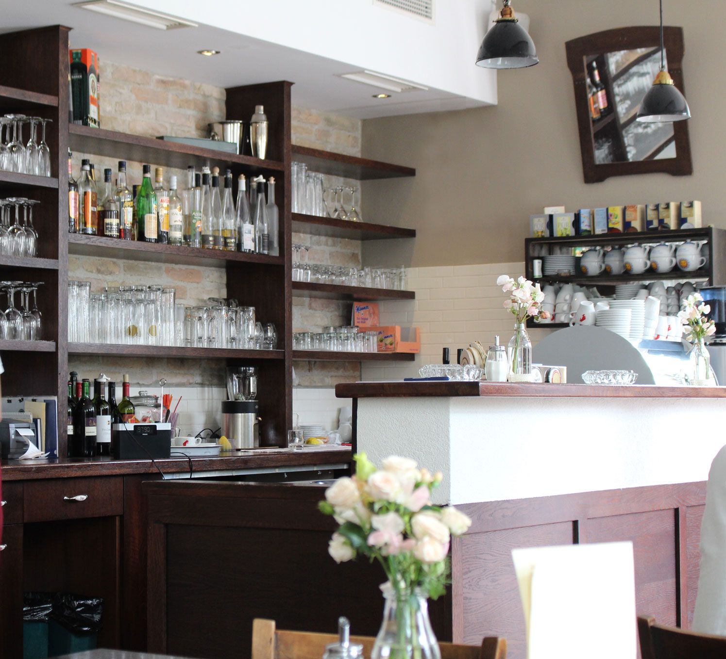 Pohled do interiéru baru s policemi plnými sklenic a lahví, květiny na pultu.