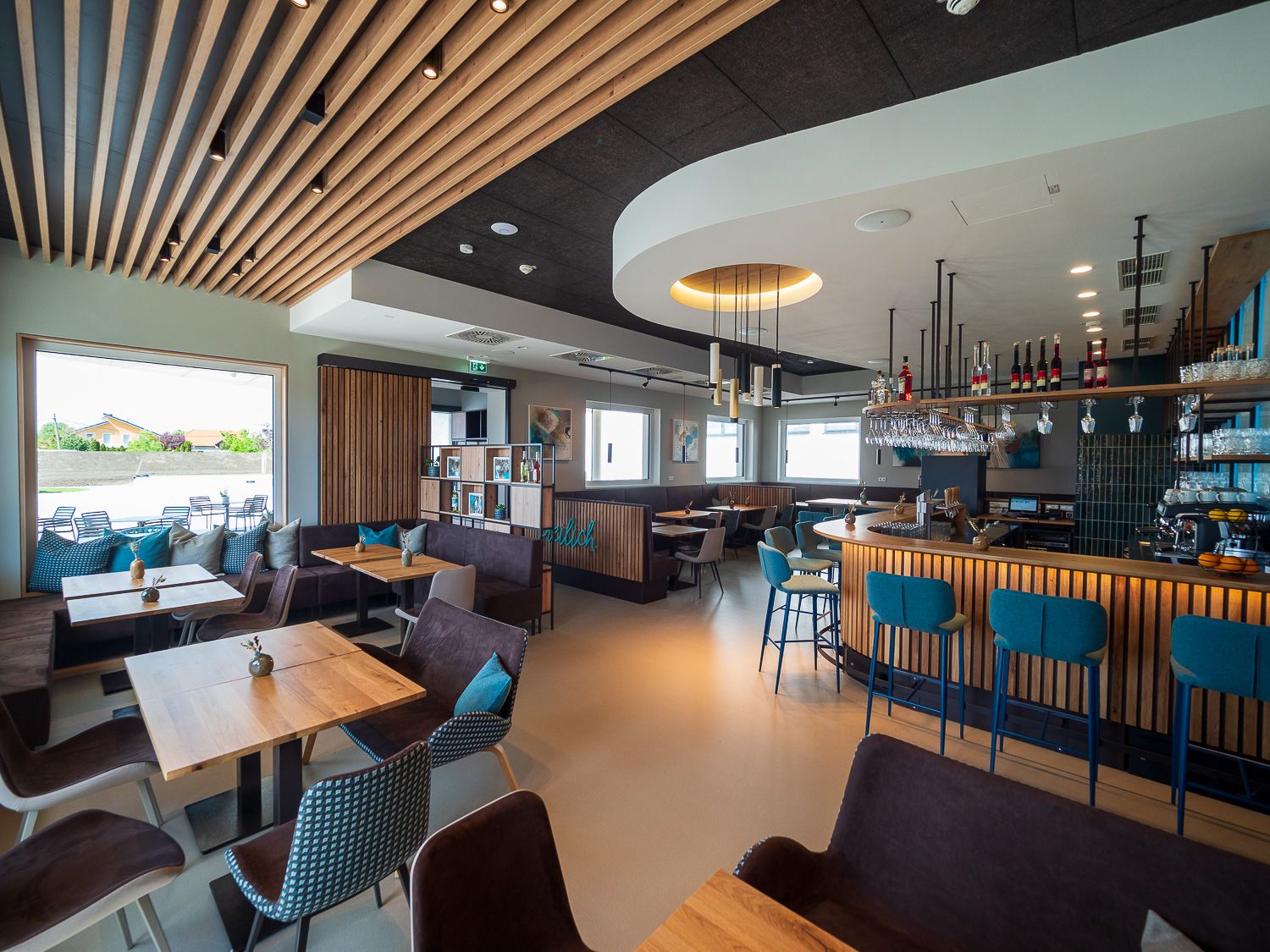 Moderní bistro s dřevěným nábytkem, barem a velkými okny.