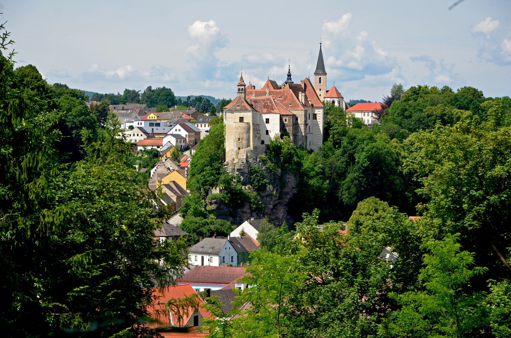 Pohled na město Raabs s hradem na kopci, obklopené stromy a domy.