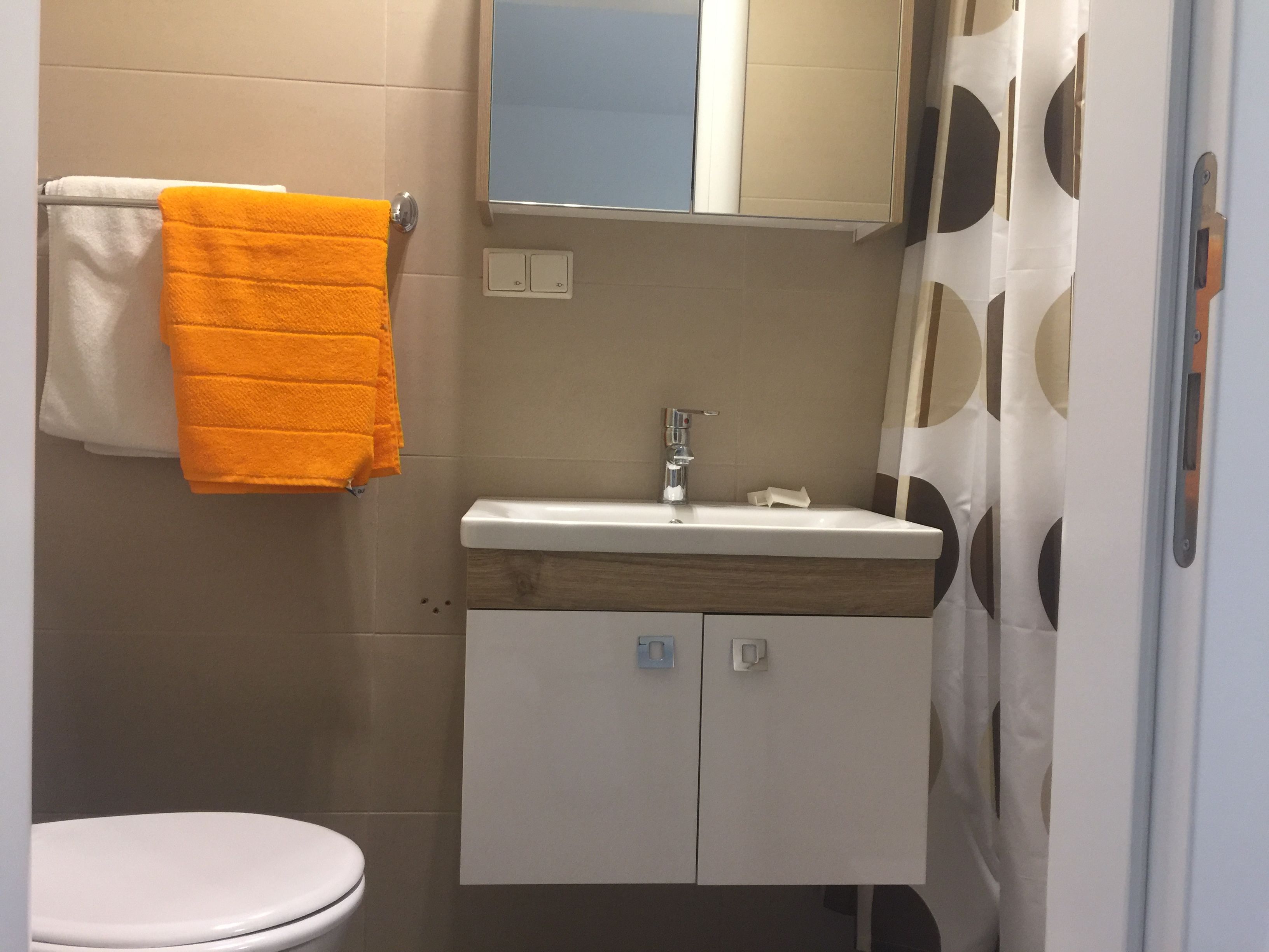 Malá koupelna s umyvadlem, zrcadlem, sprchovým závěsem a ručníky.
