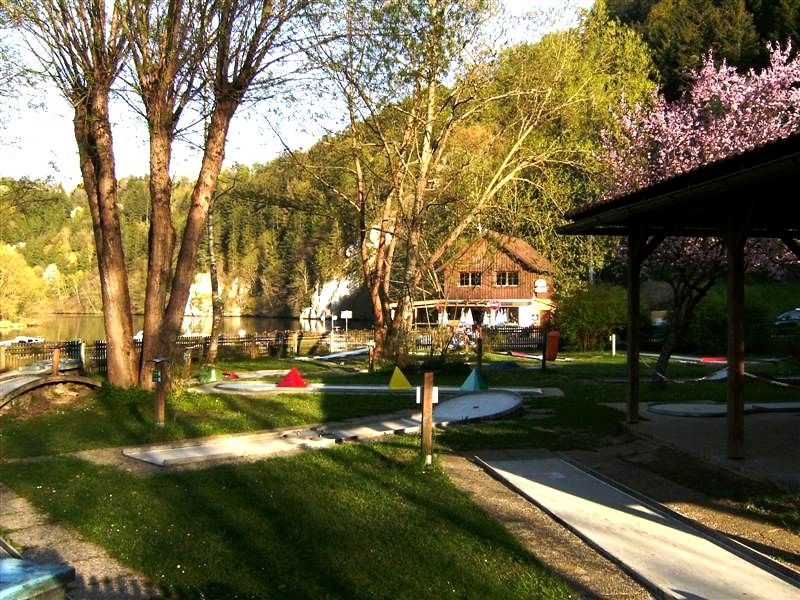 Miniaturní golfové hřiště se stromy a budovou v pozadí.