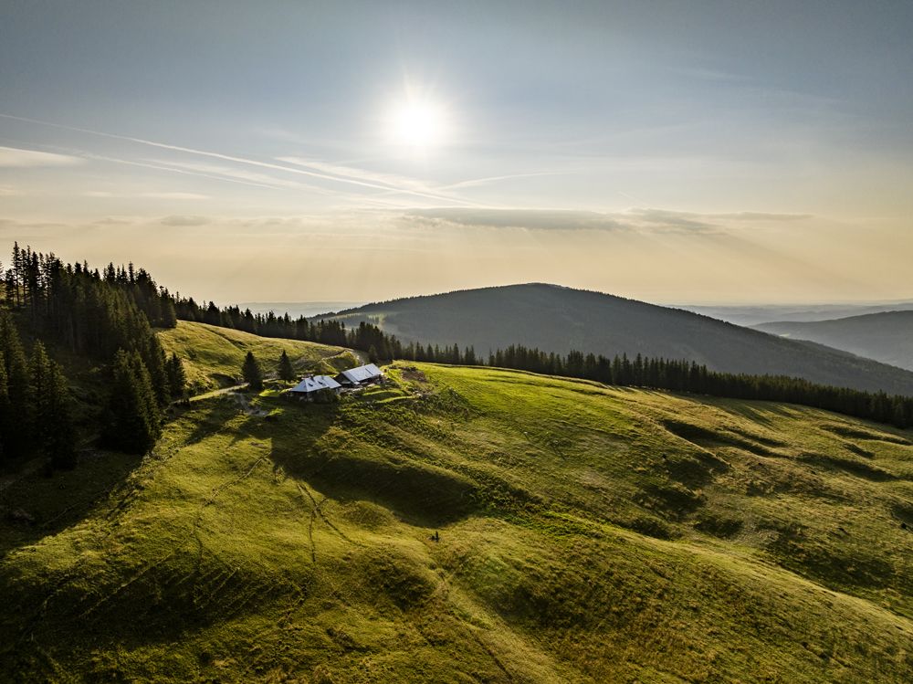 Krajina se zelenými kopci, lesem a budovou pod sluncem.