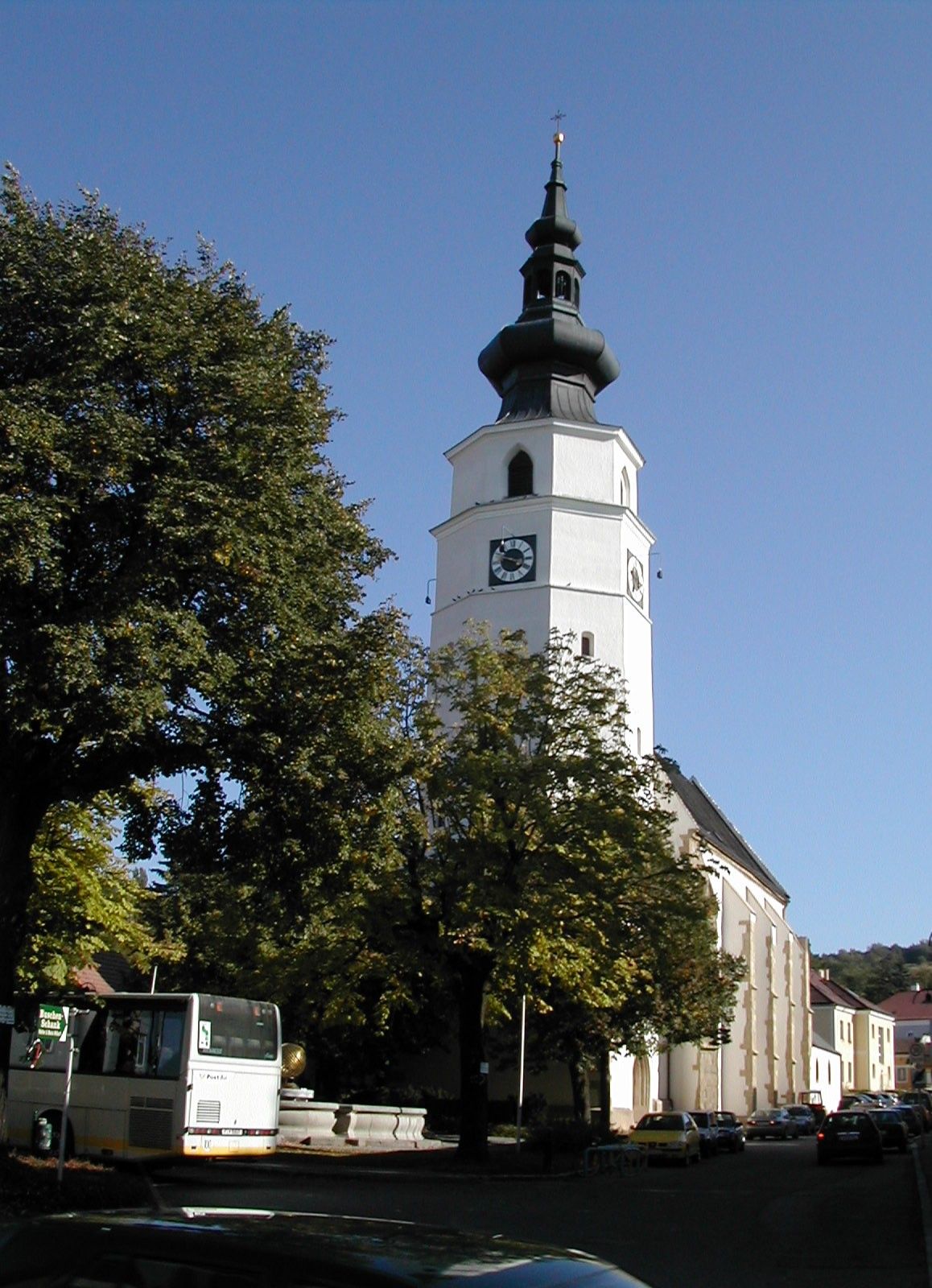Farní kostel Königstetten s věží a stromy v popředí.