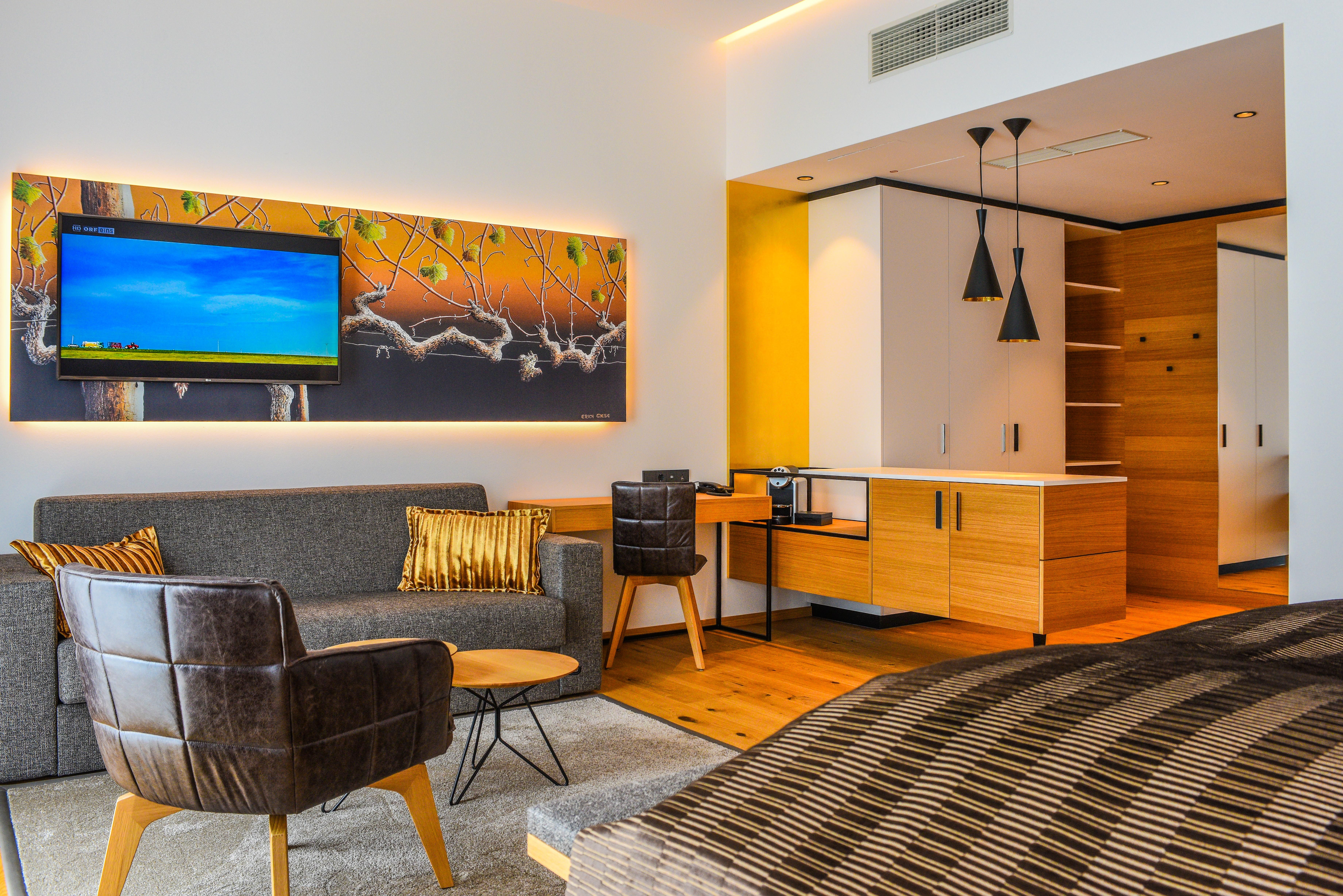 Moderní hotelové apartmá s pohovkou, křeslem, TV a kuchyňským koutem.