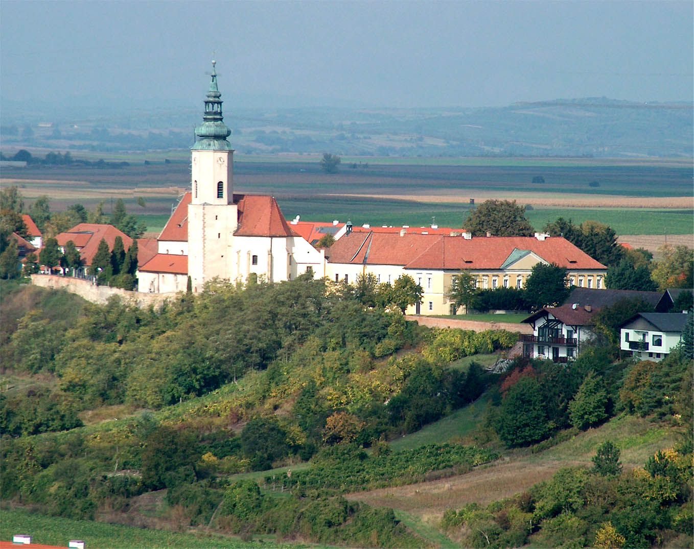Farní kostel svaté Agáty na kopci s okolními budovami a krajinou v pozadí.