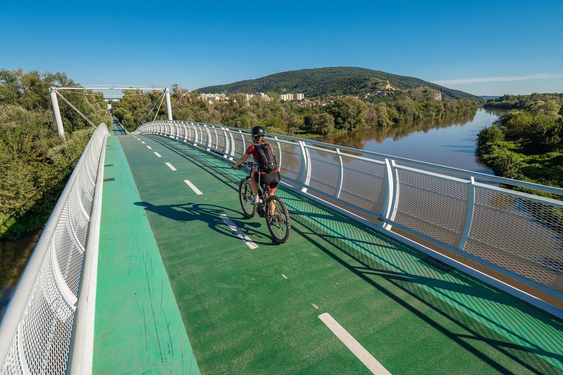 Most svobody se majestátně táhne přes klidnou řeku obklopenou bujnou zelení a kopci. Cyklisté si užívají čerstvého vzduchu a úchvatných výhledů a zároveň prožívají spojení přírody a kultury. Ideální místo pro nezapomenutelný výhled a hodiny odpočinku v přírodě.